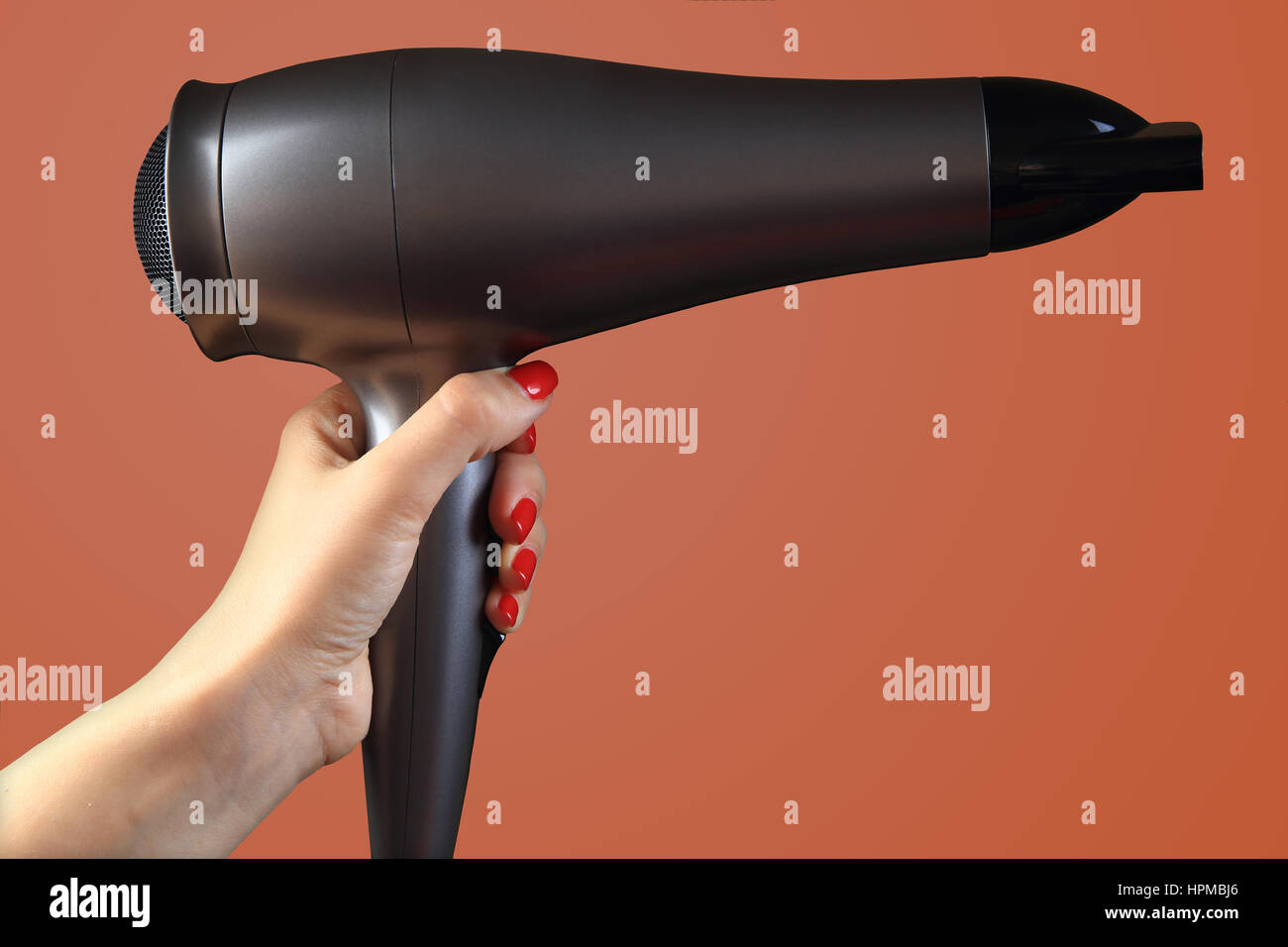 Fön in der Hand auf farbigem Hintergrund. Hand mit roten Nägeln. Stockfoto