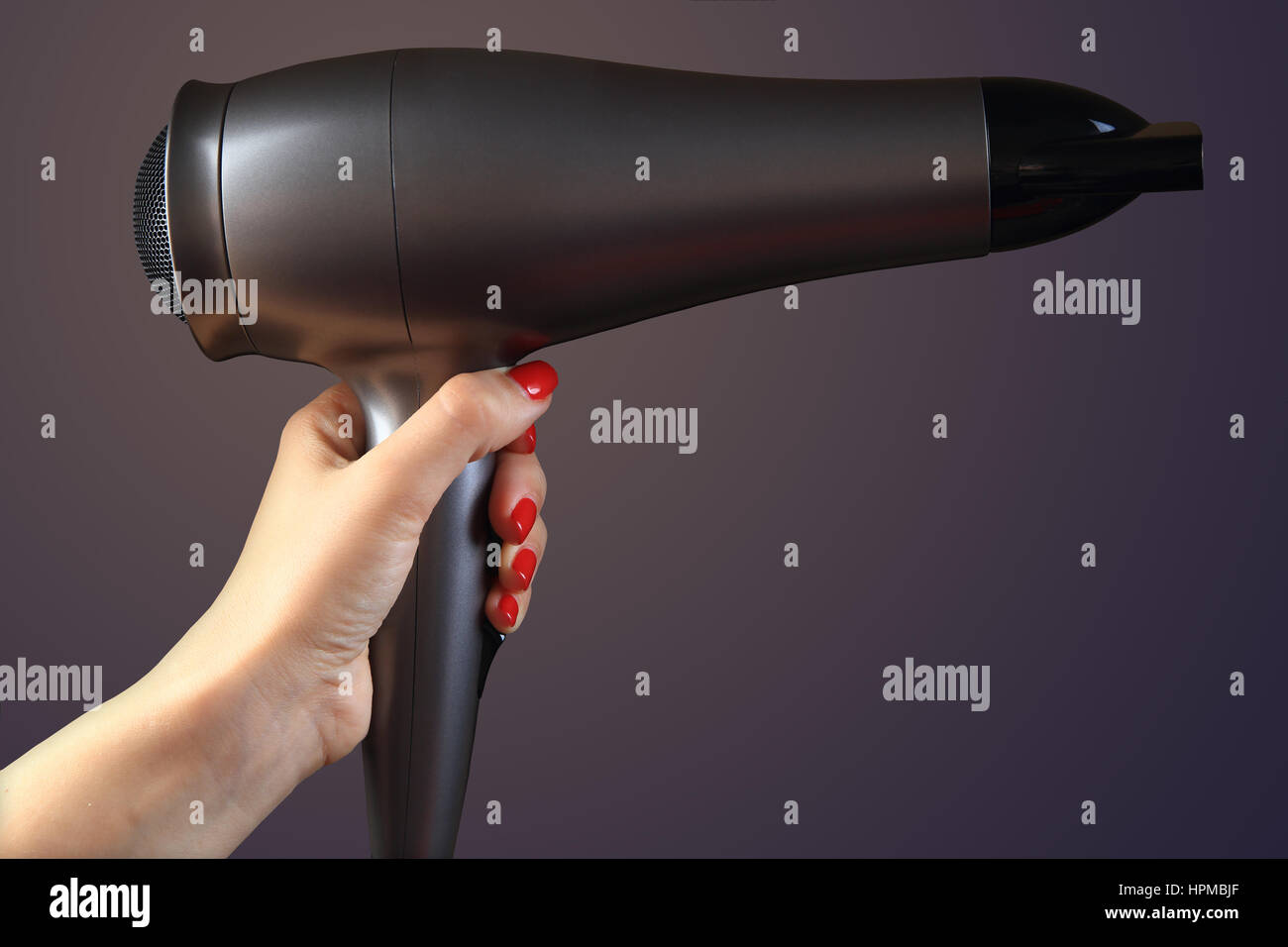 Haartrockner in Frau hand auf farbigem Hintergrund. Hand mit roten Nägeln. Stockfoto