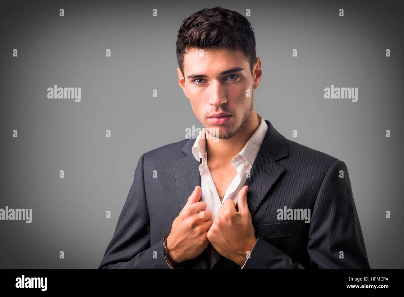 Junger Geschäftsmann zuversichtlich posieren vor der Kamera, tragen Business-Anzug ohne Krawatte mit Hemd am Hals, geöffnet auf dunklem Hintergrund Stockfoto