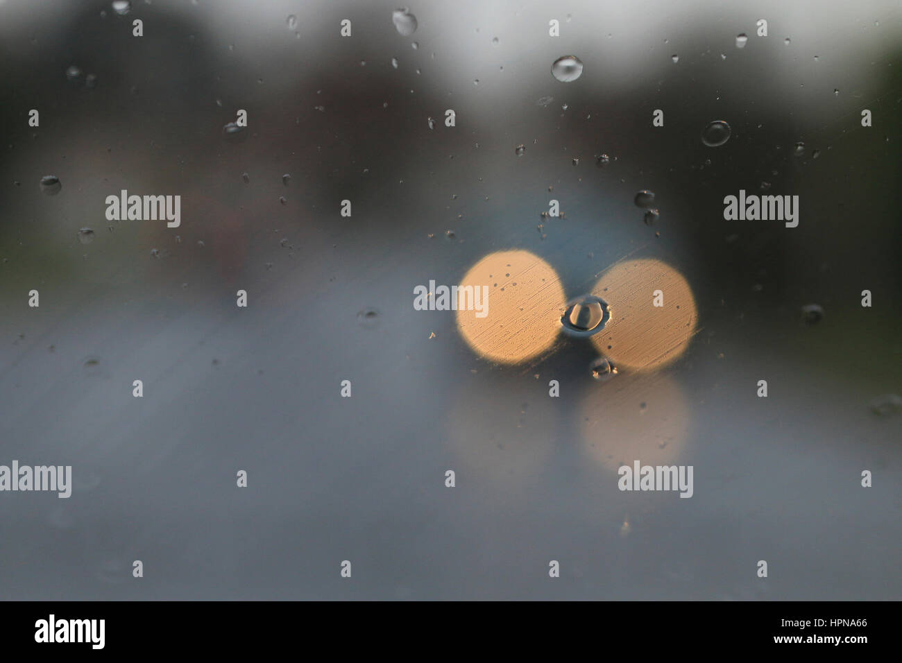 Scheinwerfer des entgegenkommenden Verkehrs durch Regen auf einer Windschutzscheibe gesehen Stockfoto
