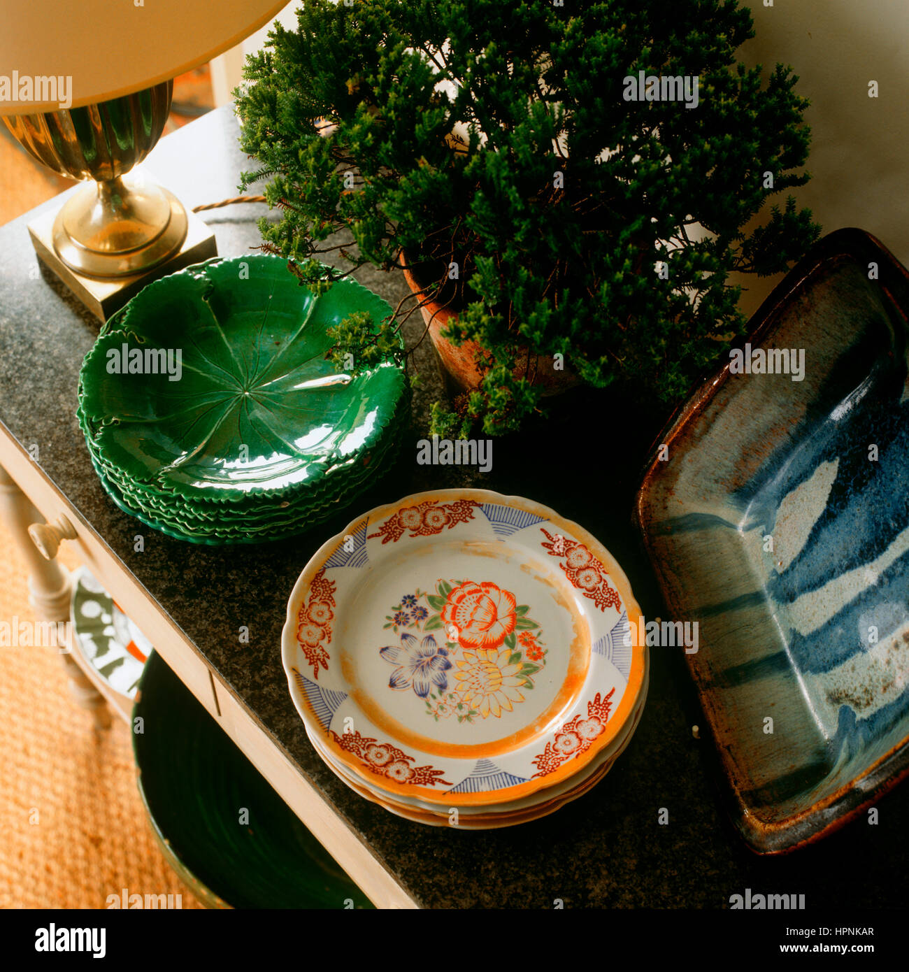 "Ein Beistelltisch mit Platten, eine Topfpflanze und eine Tischlampe." Stockfoto