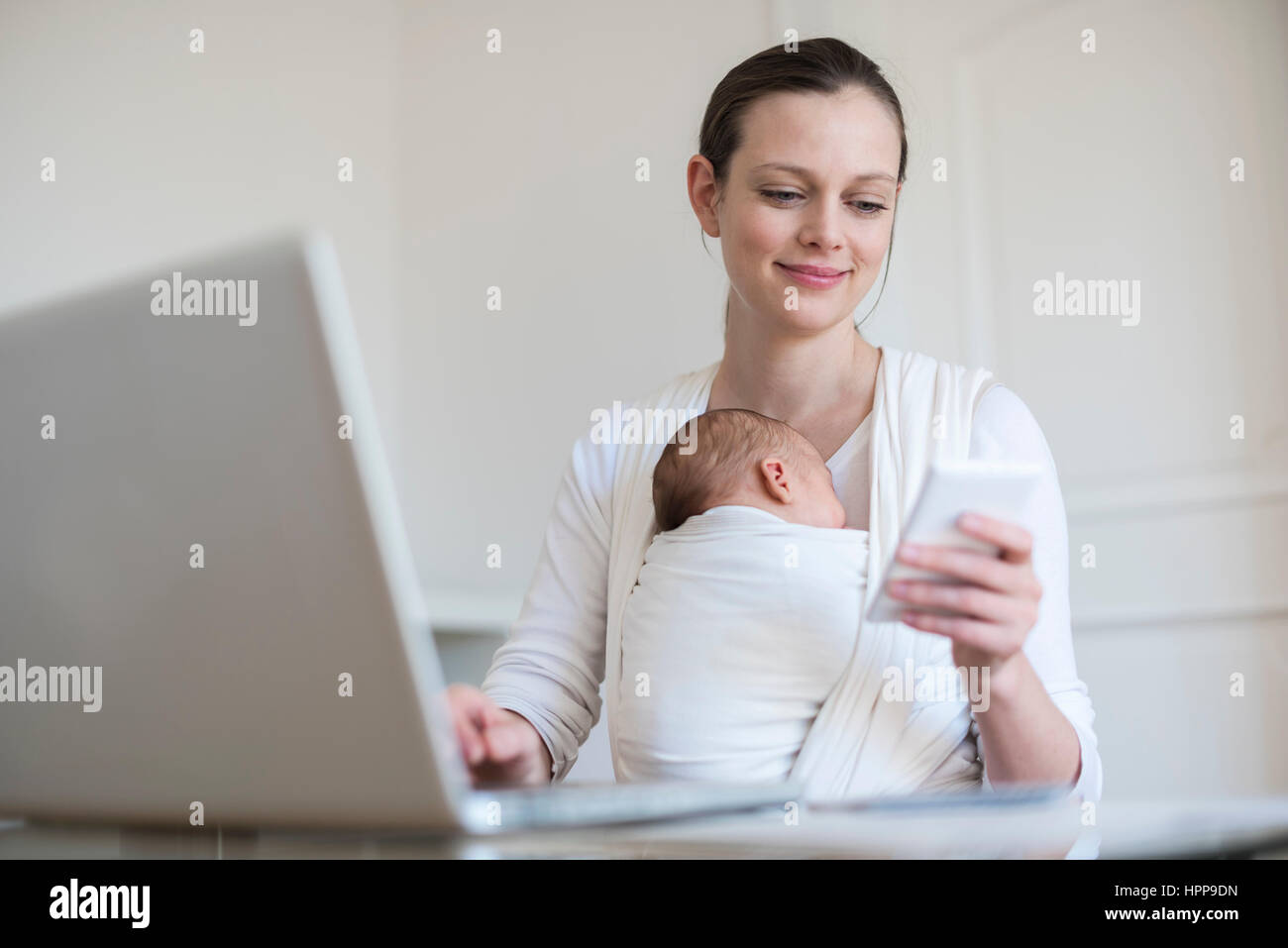 Mutter mit Baby Girl in Schlinge von zu Hause aus arbeiten Stockfoto