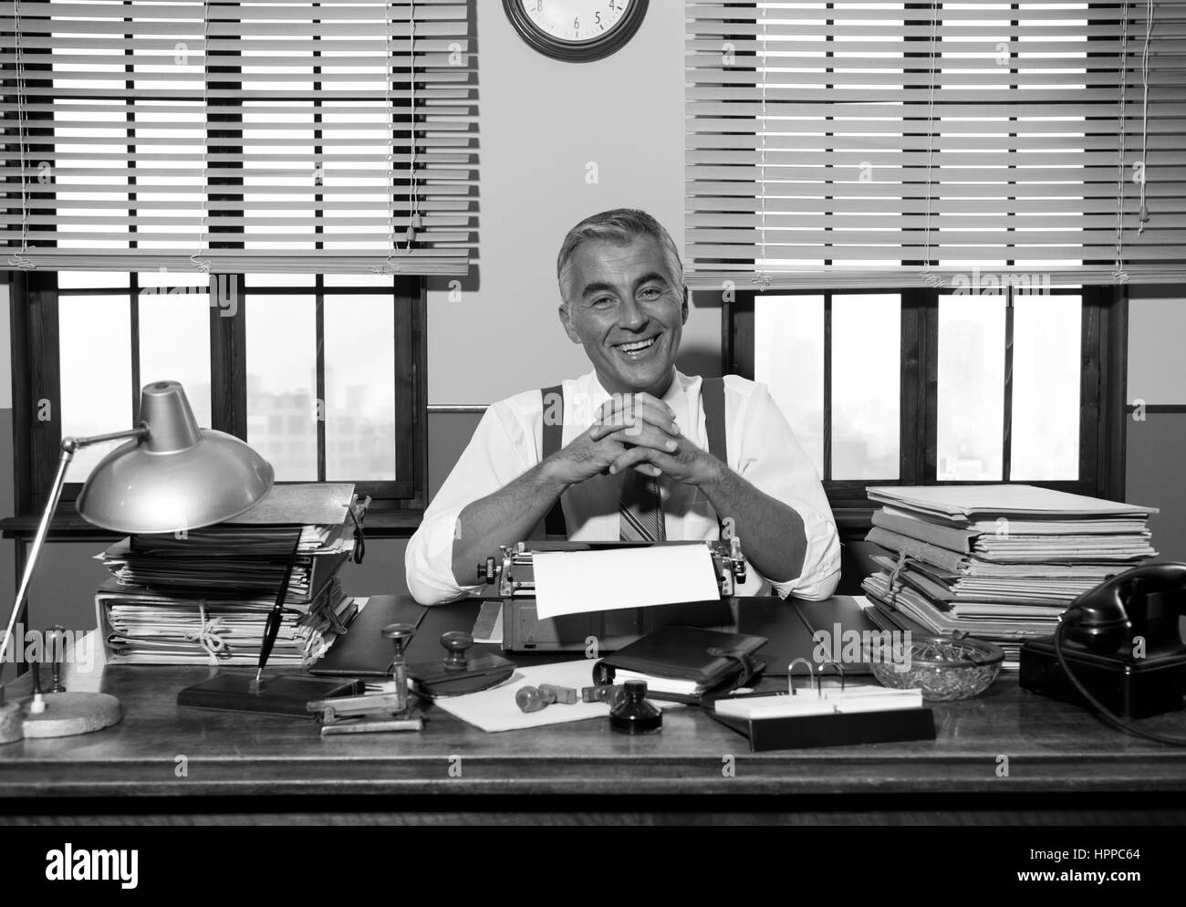 Lächelnde Reporter arbeiten am Schreibtisch mit Vintage Schreibmaschine, 1950er-Jahre Stil. Stockfoto