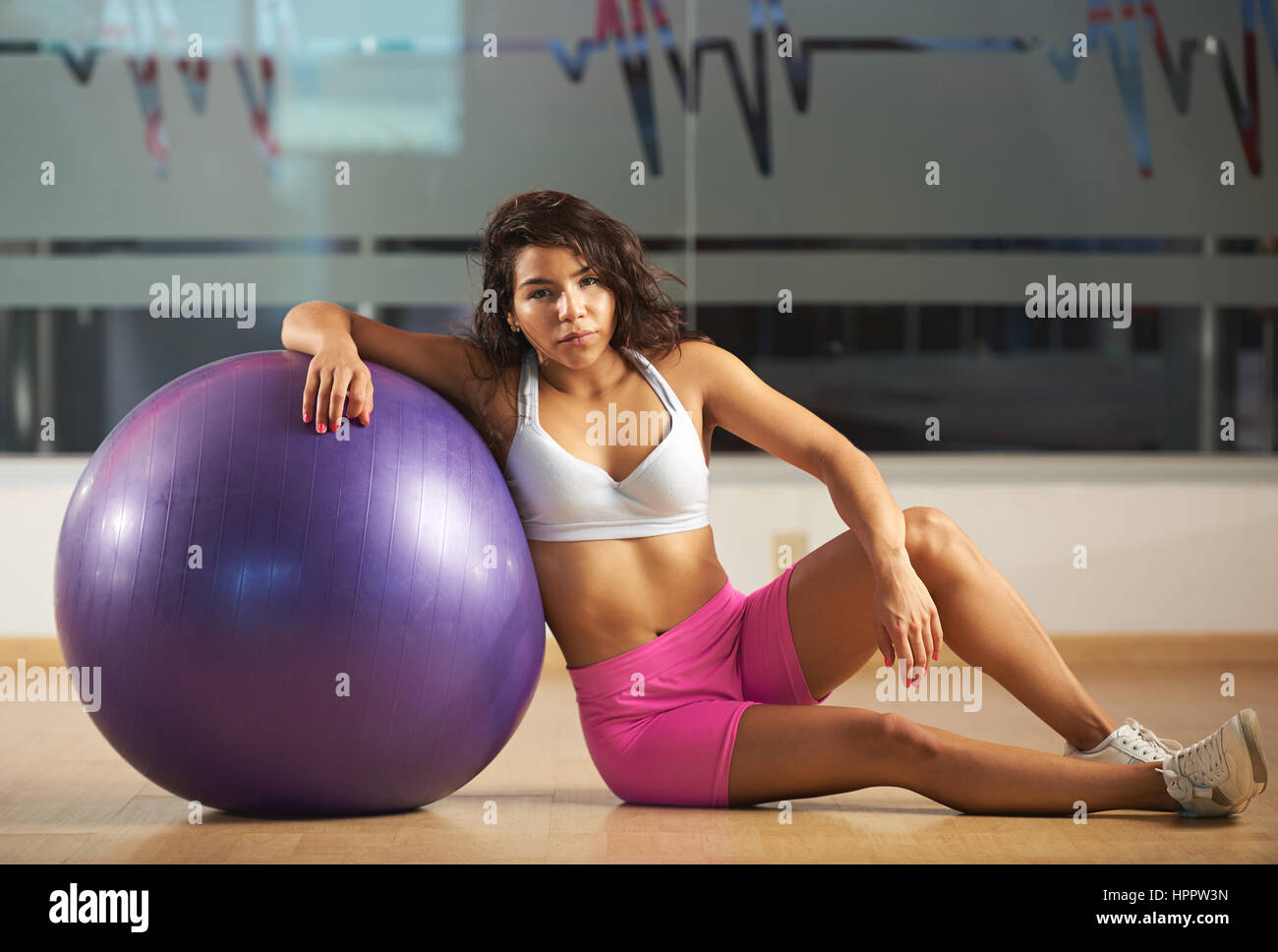 Sportliche Frau sitzt mit Fitness ball Pilates auf modernes Fitness-Studio-Hintergrund. Eine hübsche, gut in Form-Mädchen mit Fitness-ball Stockfoto