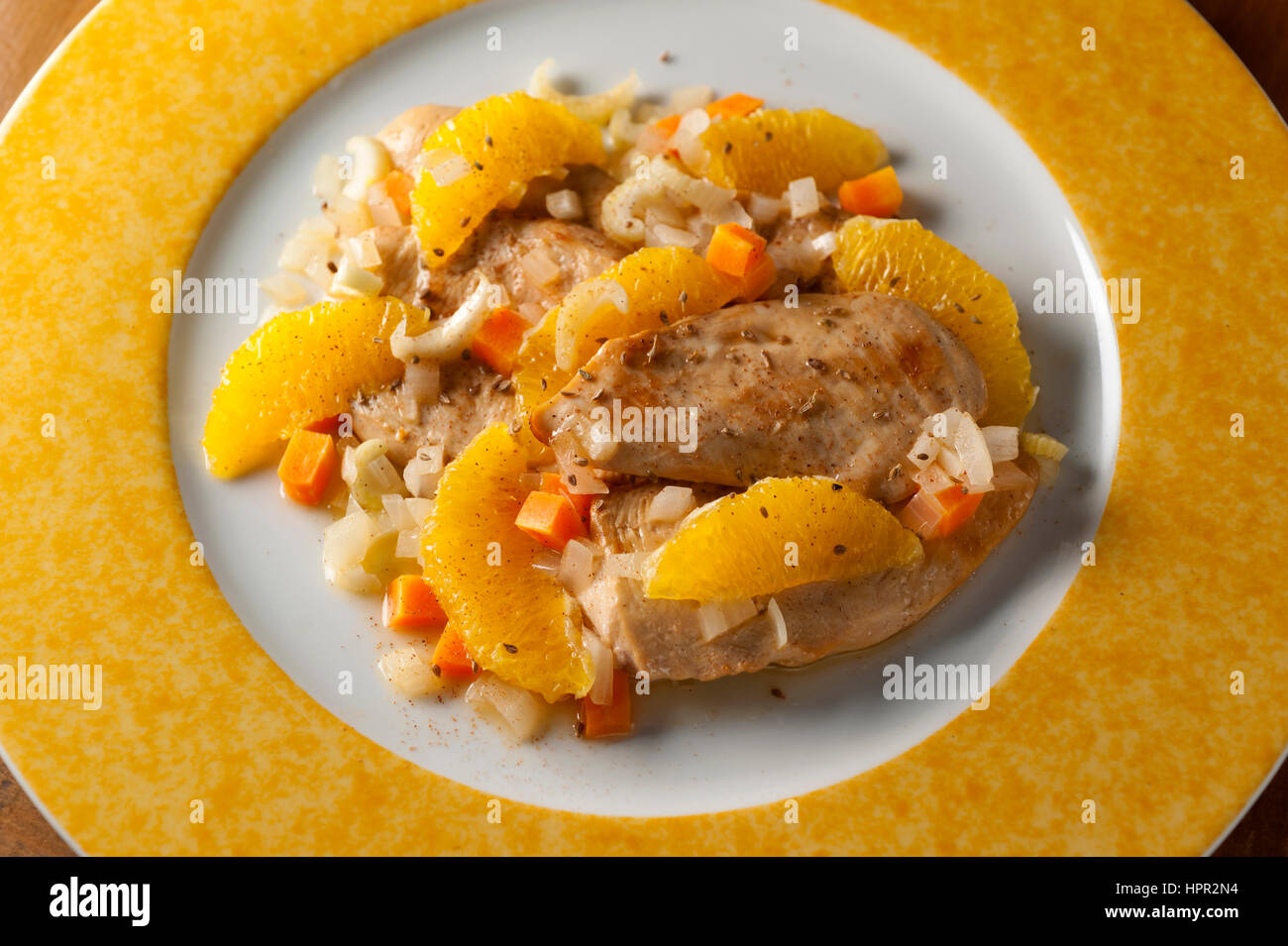 Gebratene Hühnerbrust mit Orangenscheiben und gehackte Gemüse Sauce auf einer runden weißen und gelben Platte Stockfoto