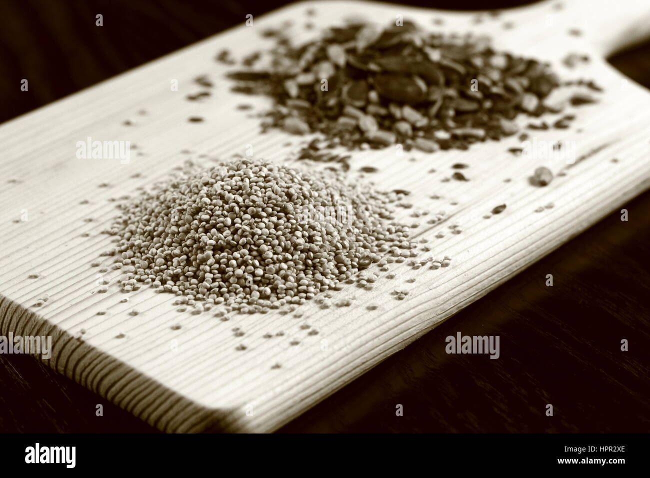 Roh (ungekocht) Quinoa (Vordergrund) und verschiedenen essbaren Samen (im Hintergrund) auf Holzbrett liegend auf dunklen Holztisch - Monochrome Sepia-Effekt Stockfoto