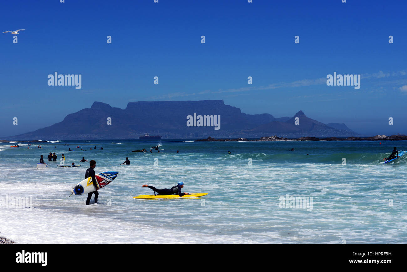 South African Surfer am Strand von Bloubergstrand mit dramatischen Blick auf den Tafelberg im Rücken. Stockfoto