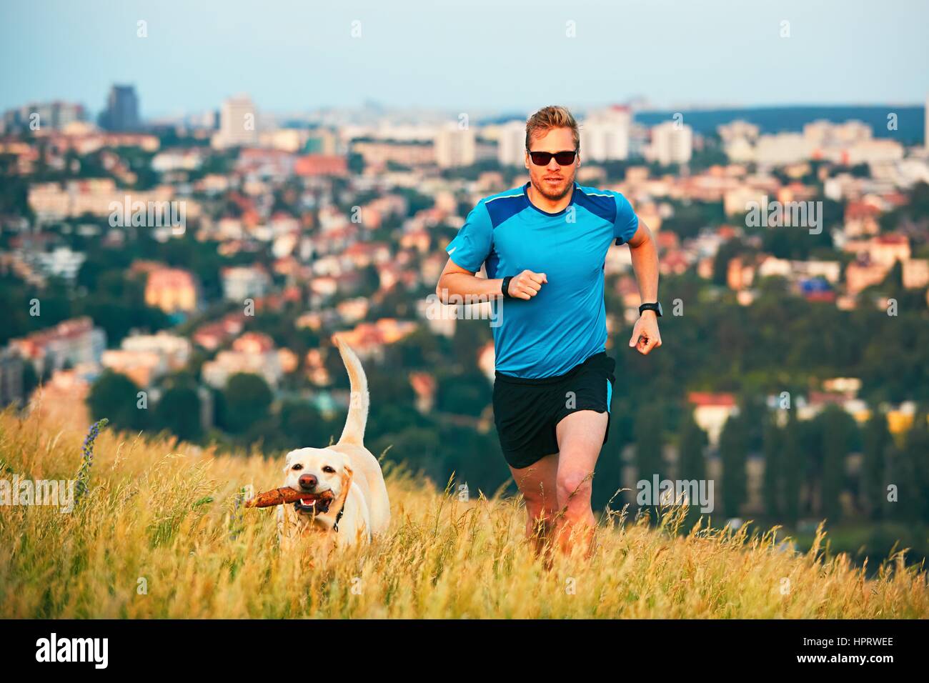 Sport-Lifestyle mit Hund. Sportlicher junger Mann und Labrador Retriever laufen auf dem Hügel außerhalb der Stadt. Prag, Tschechische Republik. Stockfoto