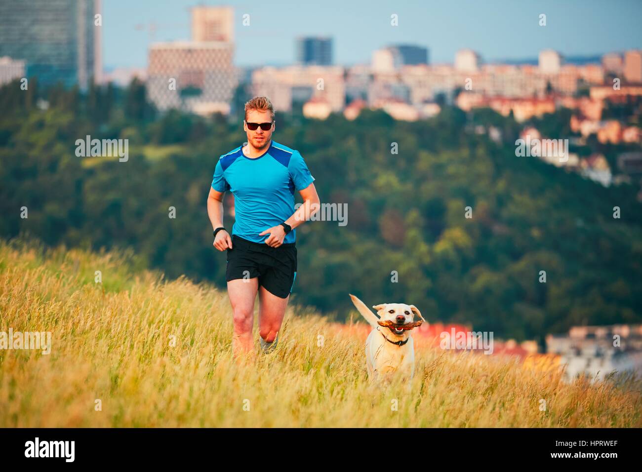 Sport-Lifestyle mit Hund. Sportlicher junger Mann und Labrador Retriever laufen auf dem Hügel außerhalb der Stadt. Prag, Tschechische Republik. Stockfoto