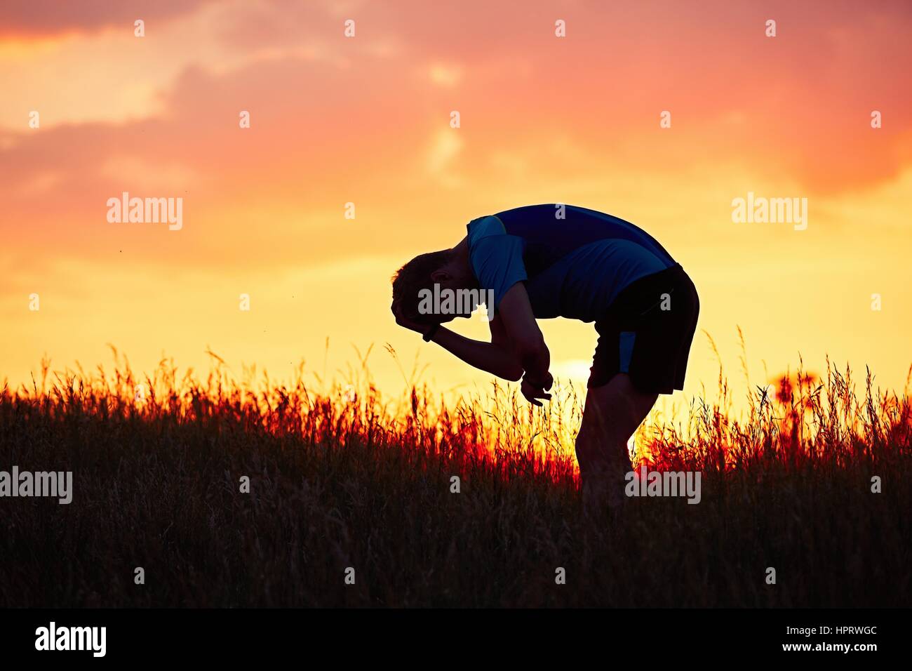 Silhouette des Läufers. Outdoor-cross-country Rennen. Nachdenklicher junger Mann nimmt Erholung nach laufen in der Natur beim goldenen Sonnenuntergang. Stockfoto