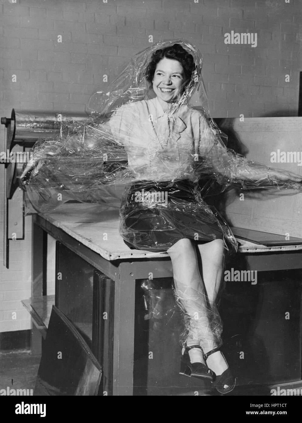 Eine Frau bedeckt in Acetat-Folie zum Laminieren sitzt auf dem Schreibtisch, 1950. Stockfoto