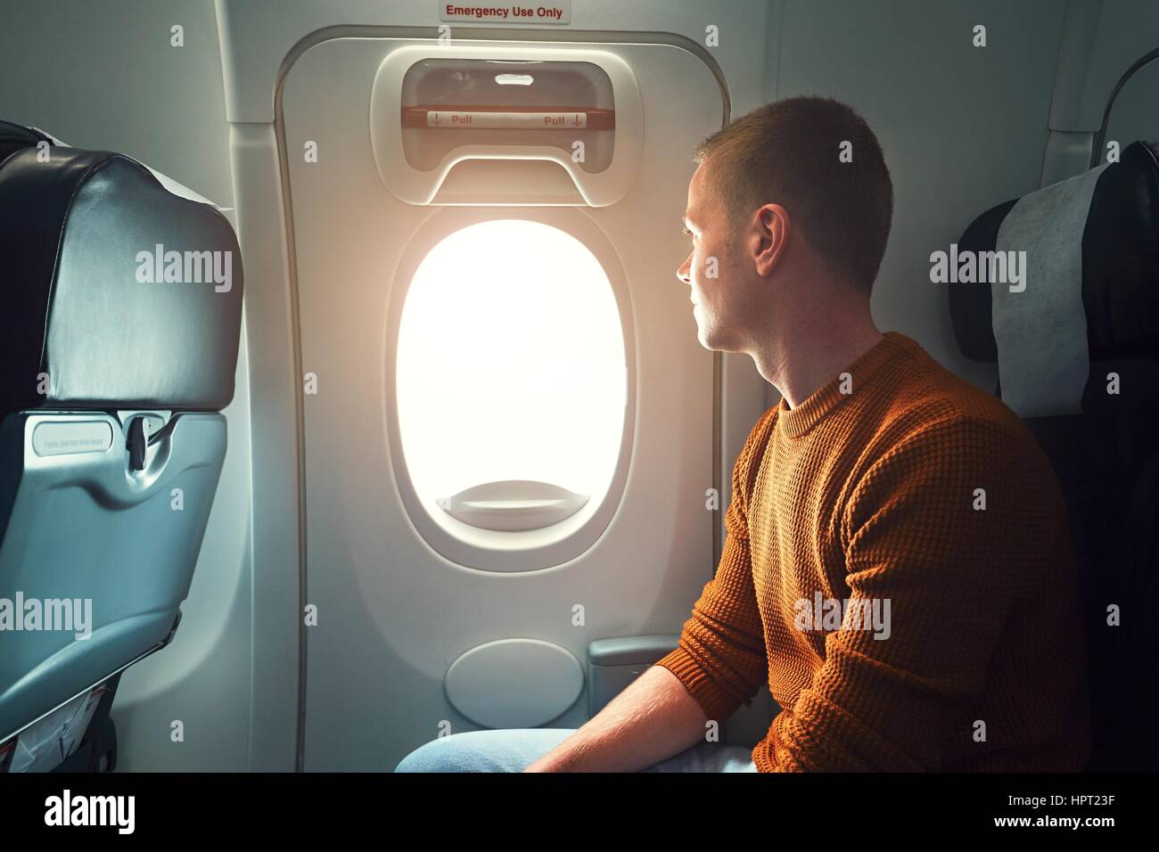 Bequeme Anreise mit dem Flugzeug. Neugierige junge Passagier Blick aus dem Fenster (Notausgang aus dem Flugzeug). Stockfoto