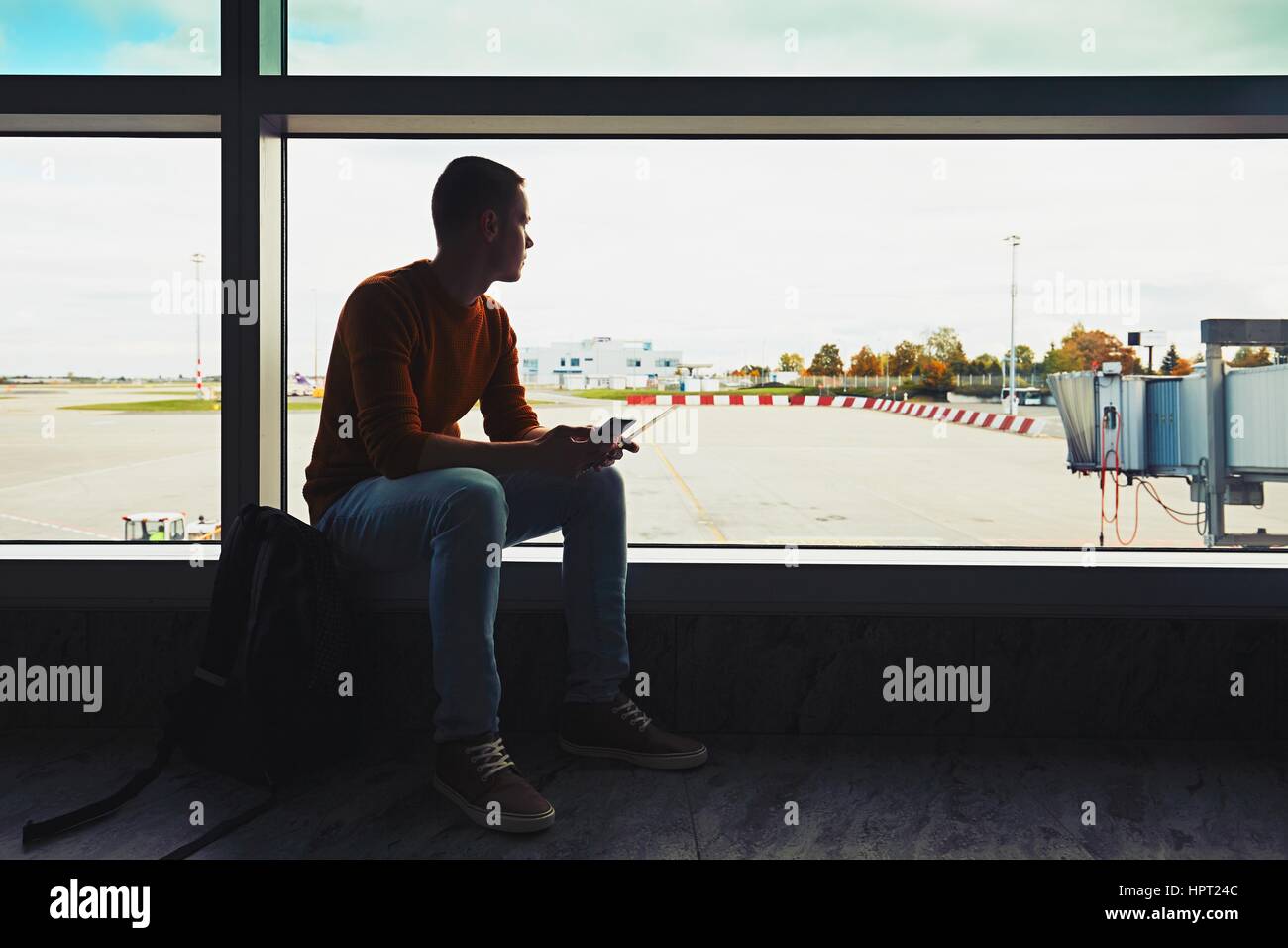 Silhouette des jungen Mannes mit Handy und Boarding pass in der hand warten im Flughafen terminal zum Flugzeug. Stockfoto