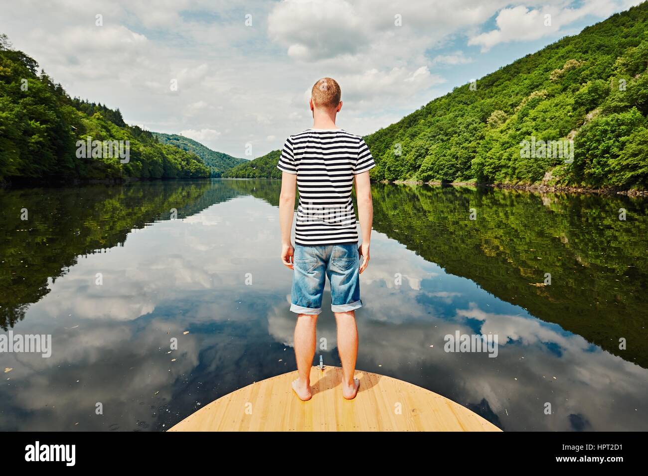 Urlaubsreise auf dem Fluss. Gut aussehender Mann mit blau-weiß gestreiften Hemd auf dem Bug des Bootes. Vltava (Moldau) in der Nähe von Prag, Tschechische Republik Stockfoto