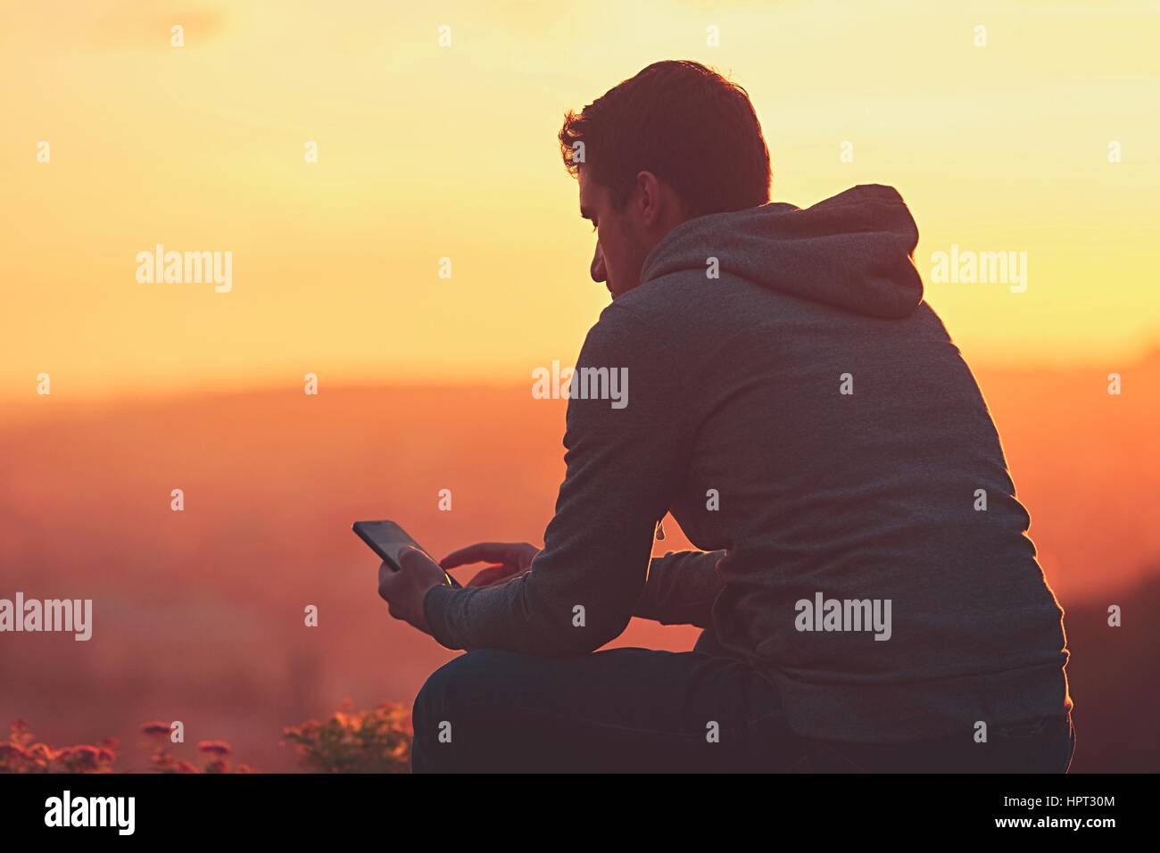 Junger Mann mit Handy auf den Sonnenaufgang. Stockfoto