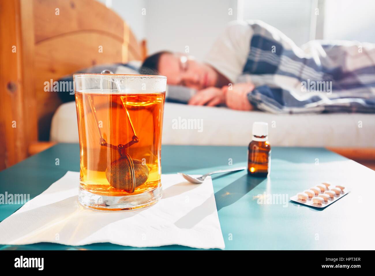 Kranker Mann liegt im Bett unter der Decke. Selektiven Fokus auf den heißen Tee und Medizin auf dem Tisch. Stockfoto
