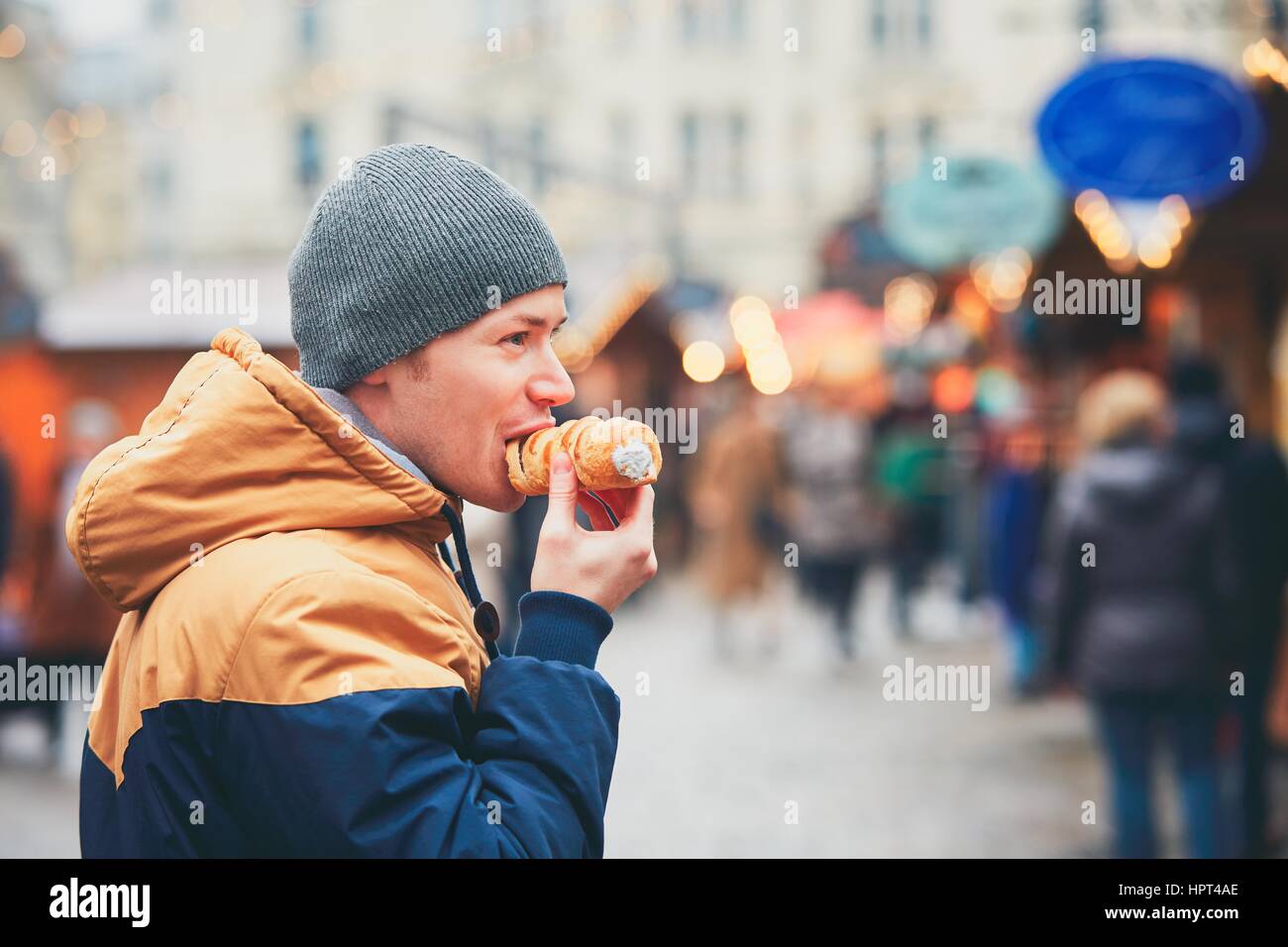 Junger Mann Essen Blätterteig Rollen mit Sahne auf Weihnachtsmarkt, Wien, Österreich Stockfoto