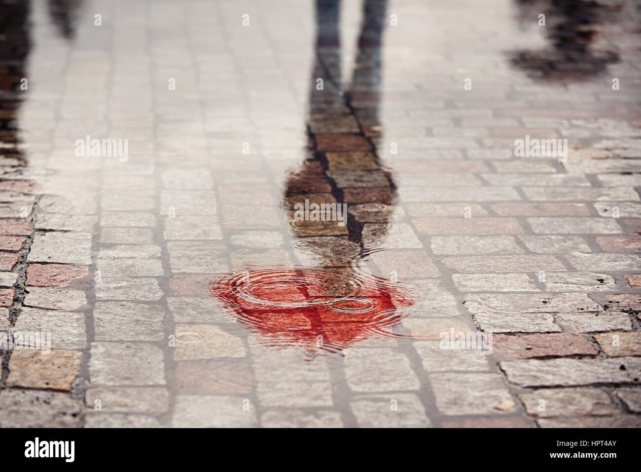 Regnerischen Tag. Reflexion der junger Mann mit roten Regenschirm in Pfütze auf der Stadtstraße bei Regen. Stockfoto