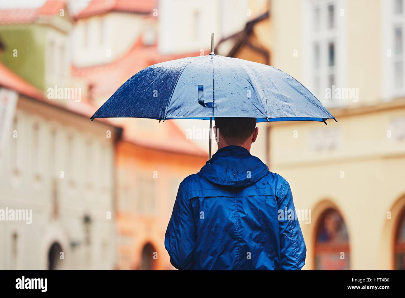 Regnerischen Tag. Junger Mann hält blaue Regenschirm und Wandern in Regen. Straße von Prag, Tschechische Republik. Stockfoto