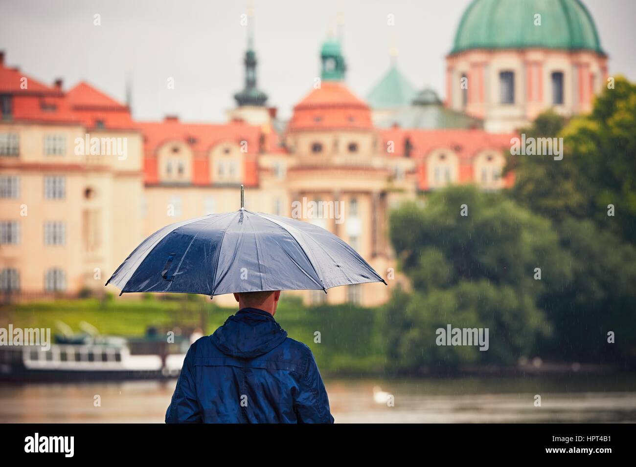 Regnerischen Tag. Junger Mann hält blaue Regenschirm und Wandern in Regen. Prag, Tschechische Republik. Stockfoto