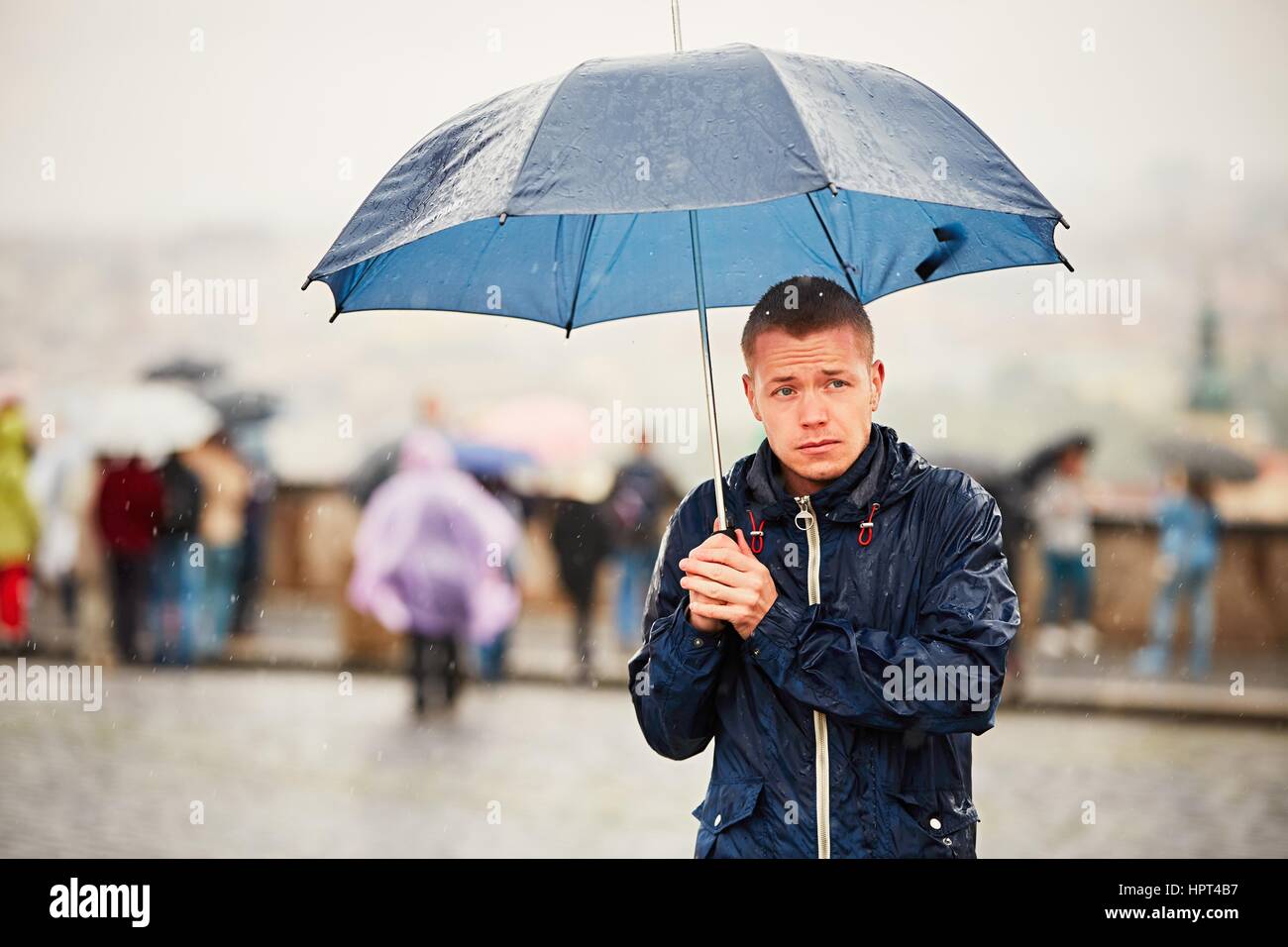 Regnerischen Tag. Junger Mann hält blaue Regenschirm und Wandern in Regen. Straße von Prag, Tschechische Republik. Stockfoto