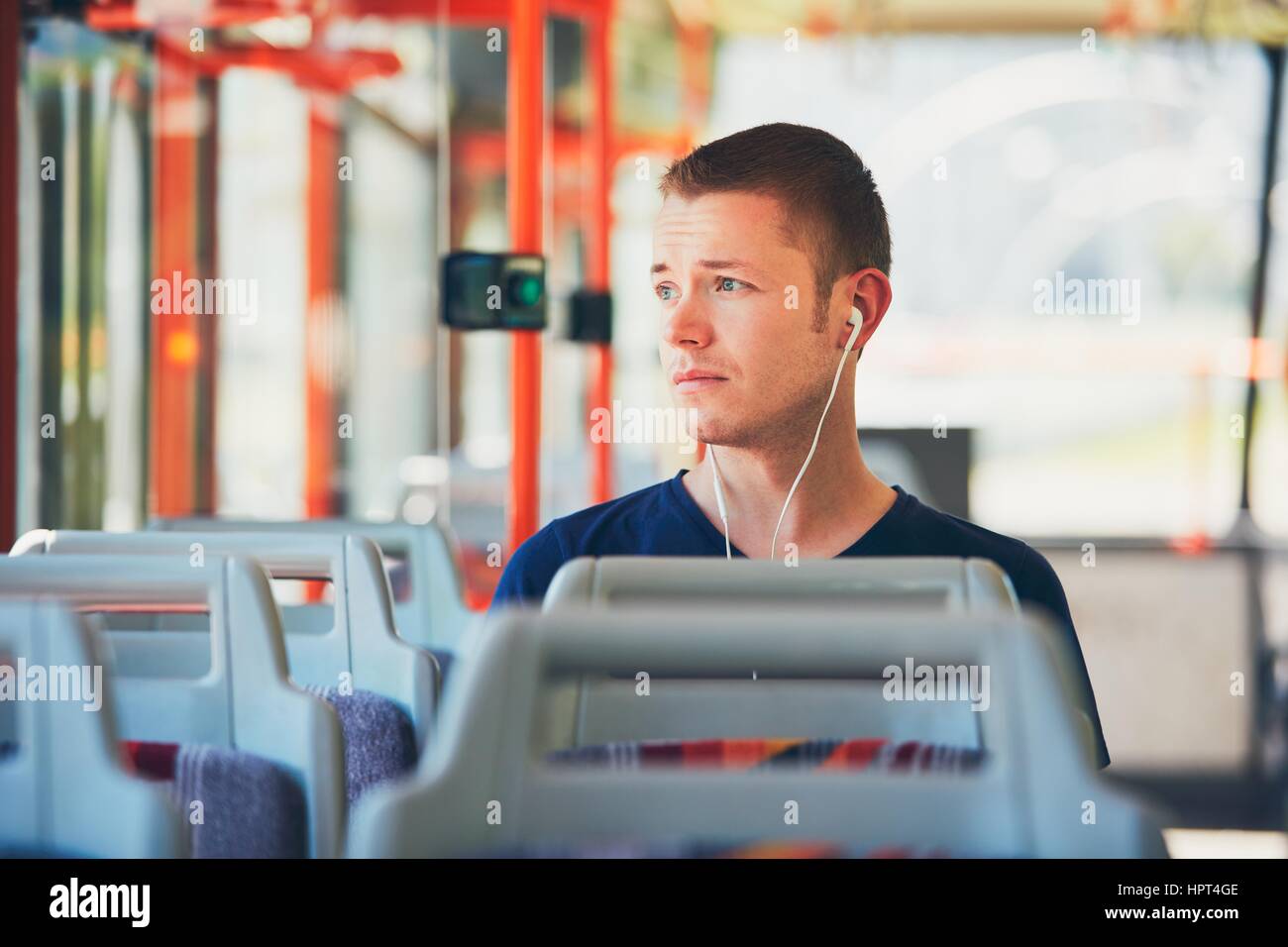 Trauriger junger Mann reist mit der Straßenbahn (Bus). Alltag und pendeln zur Arbeit mit öffentlichen Verkehrsmitteln. Mann trägt Kopfhörer und anhören von mus Stockfoto