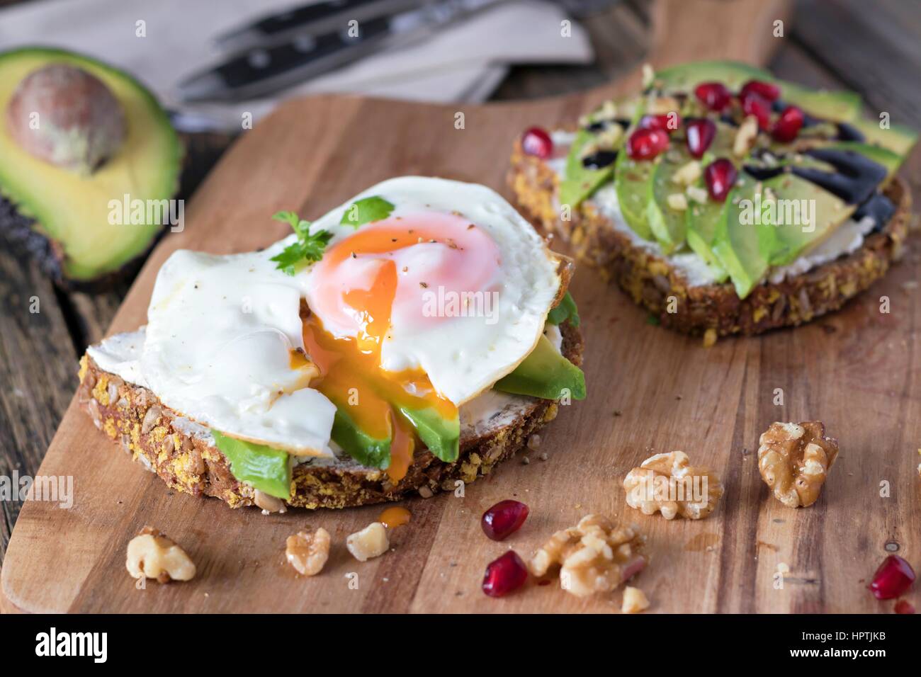 Protein Brotscheibe mit Frischkäse, Avocado in Scheiben und Spiegelei auf Holzbrett Stockfoto