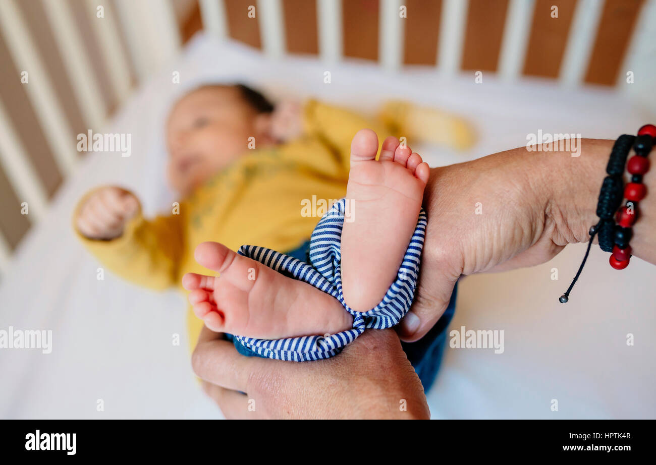 Großmutters Hände halten Babys Füße liegen in Krippe Stockfoto