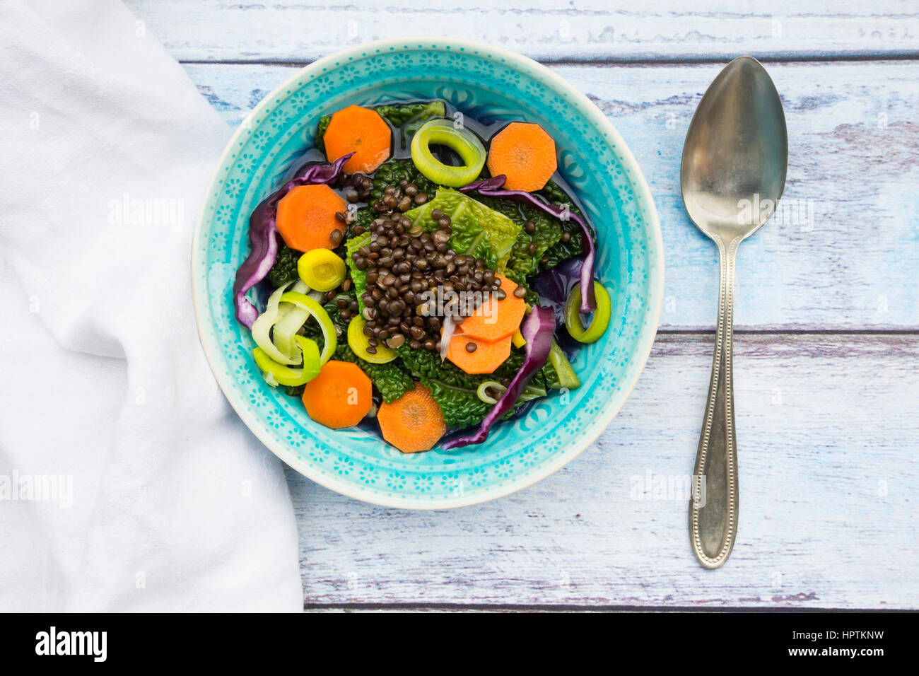 Schüssel mit Vegan-Kohl-Eintopf mit Linsen und Löffel auf Holz Stockfoto