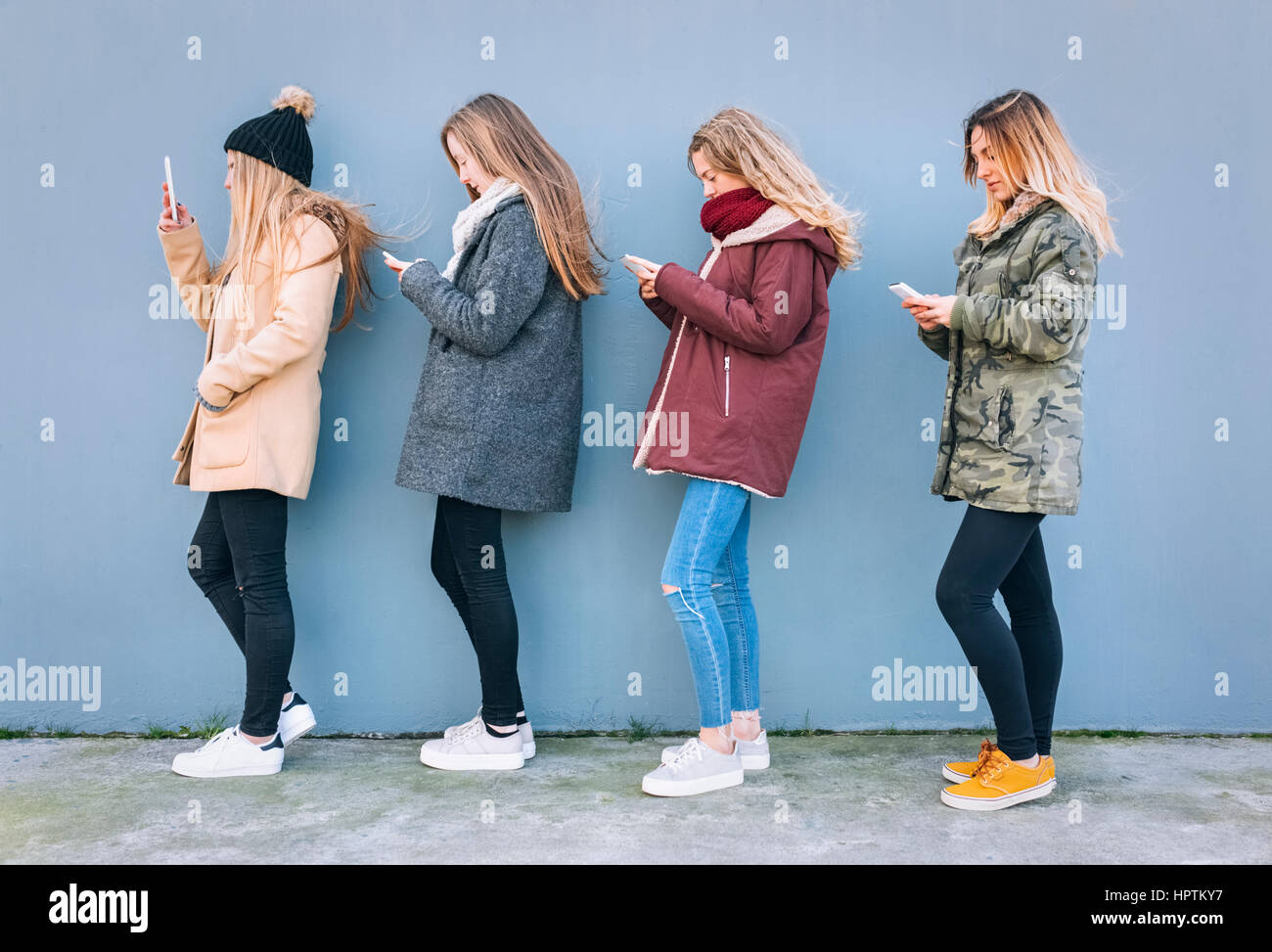 Vier junge Frauen, die in einer Reihe mit ihren Handys Stockfoto