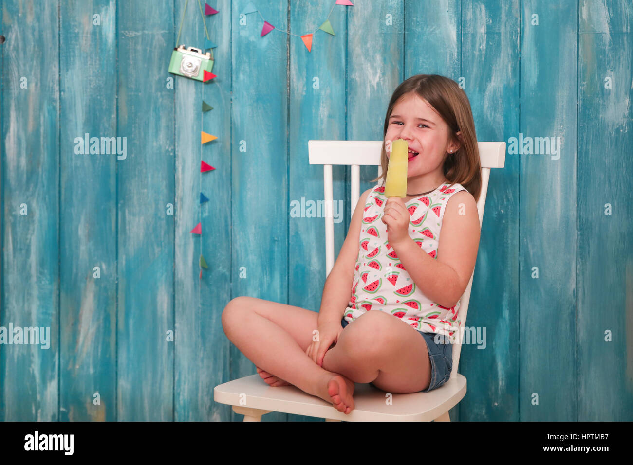 Glückliche kleine Mädchen sitzen auf Stuhl Essen Zitronen Eis am Stiel Stockfoto