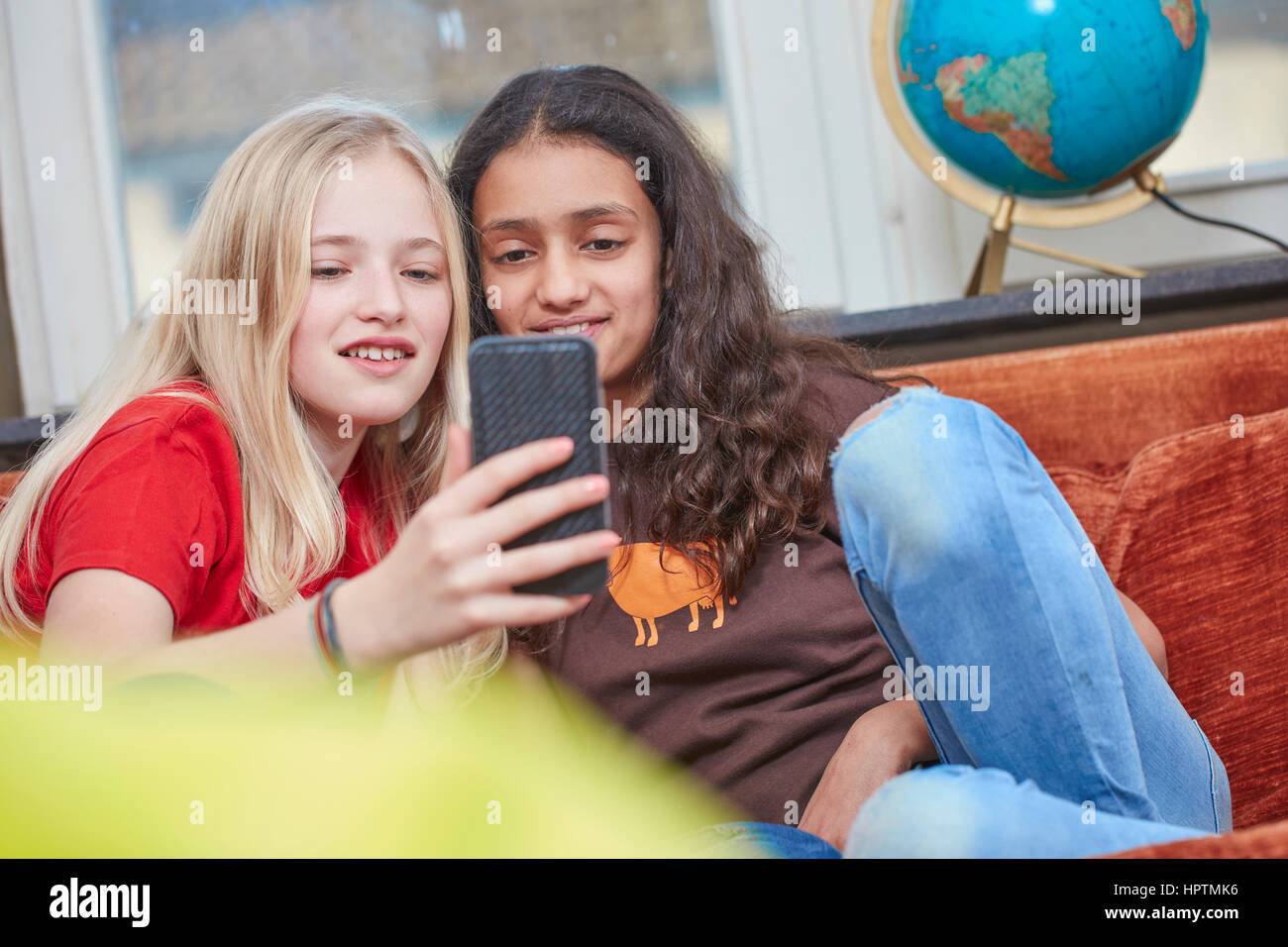 Zwei Mädchen auf Couch teilen smartphone Stockfoto