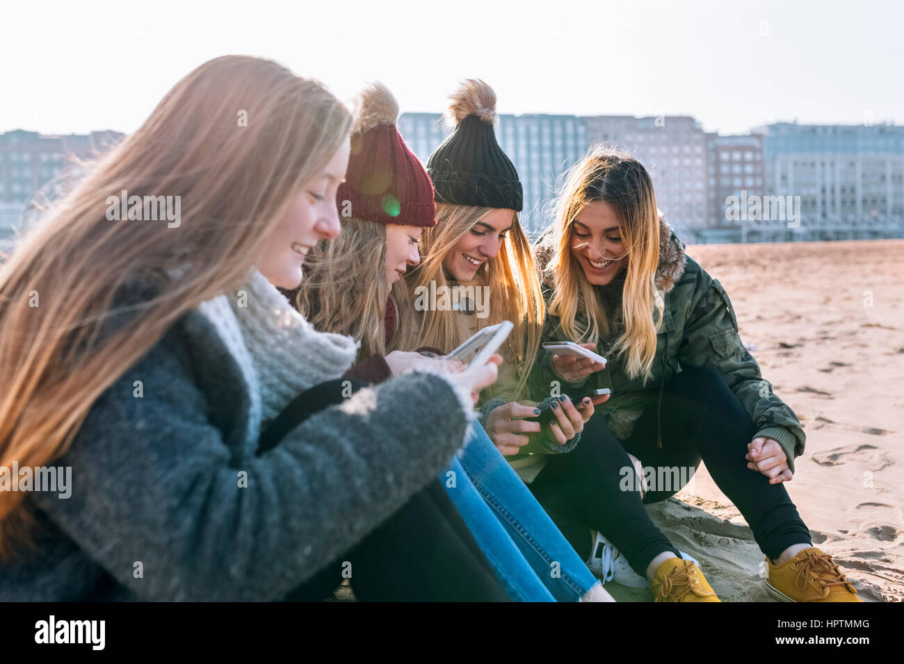 Vier Freunde sitzen auf der Strand-Text-messaging Stockfoto