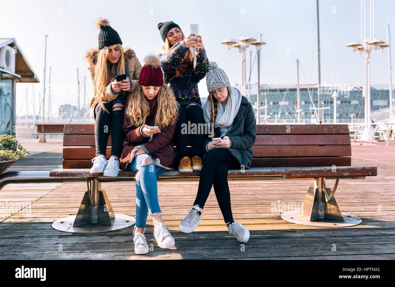 Vier junge Frauen sitzen auf einer Bank mit ihren Handys Stockfoto