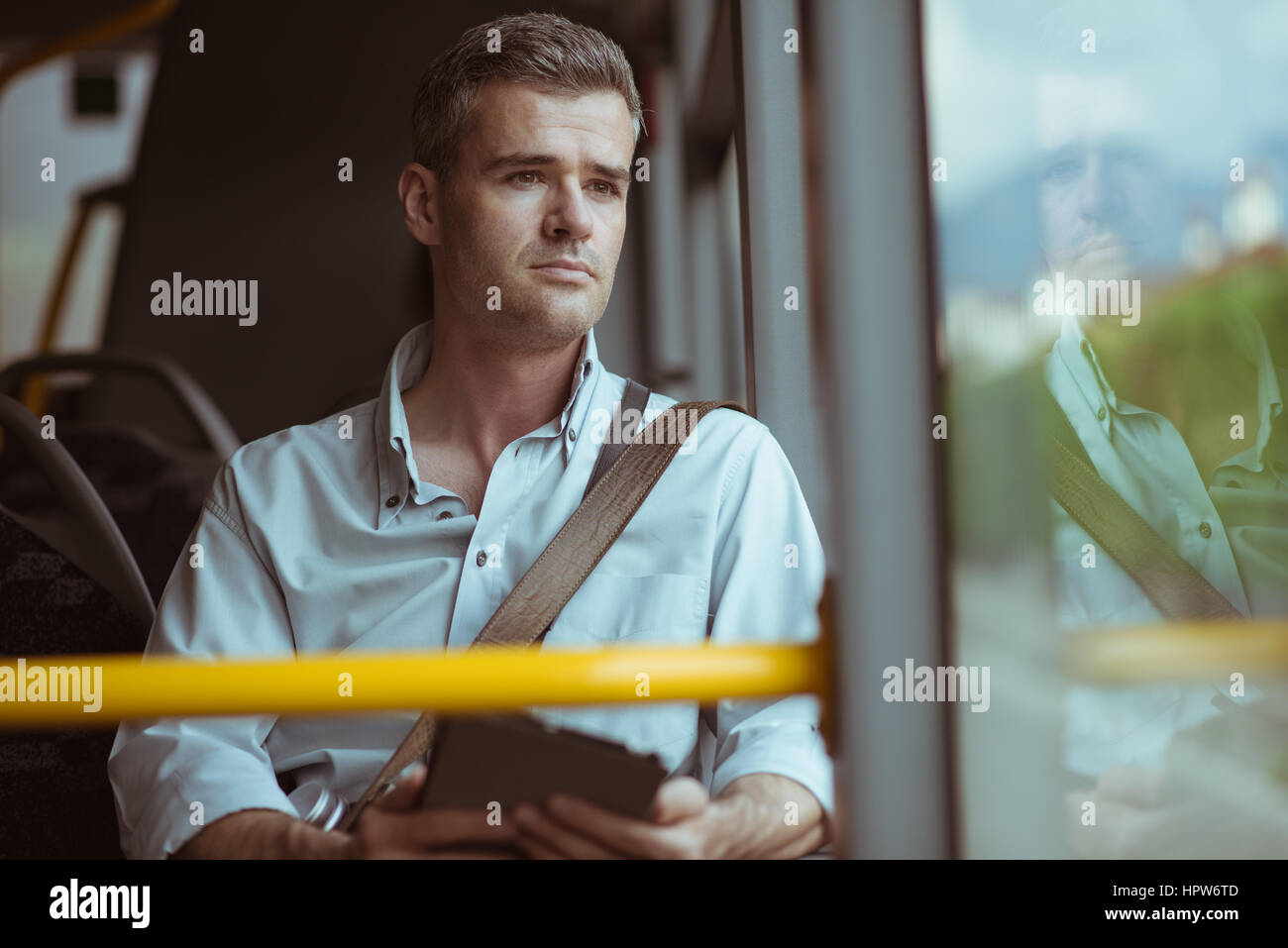 Zuversichtlich nachdenklicher Mann sitzt im Bus, er ist durch ein Fenster schaut und mit Hilfe eine digitale-Tablette Stockfoto