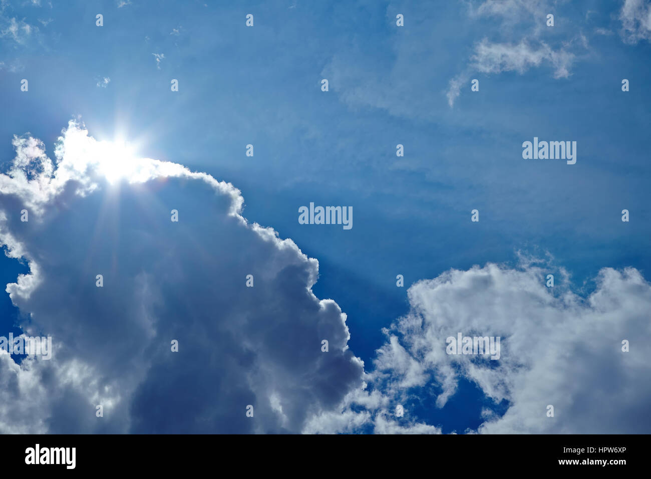 Strahlende Sonne hinter einige weiße Wolken am blauen Himmel Stockfoto
