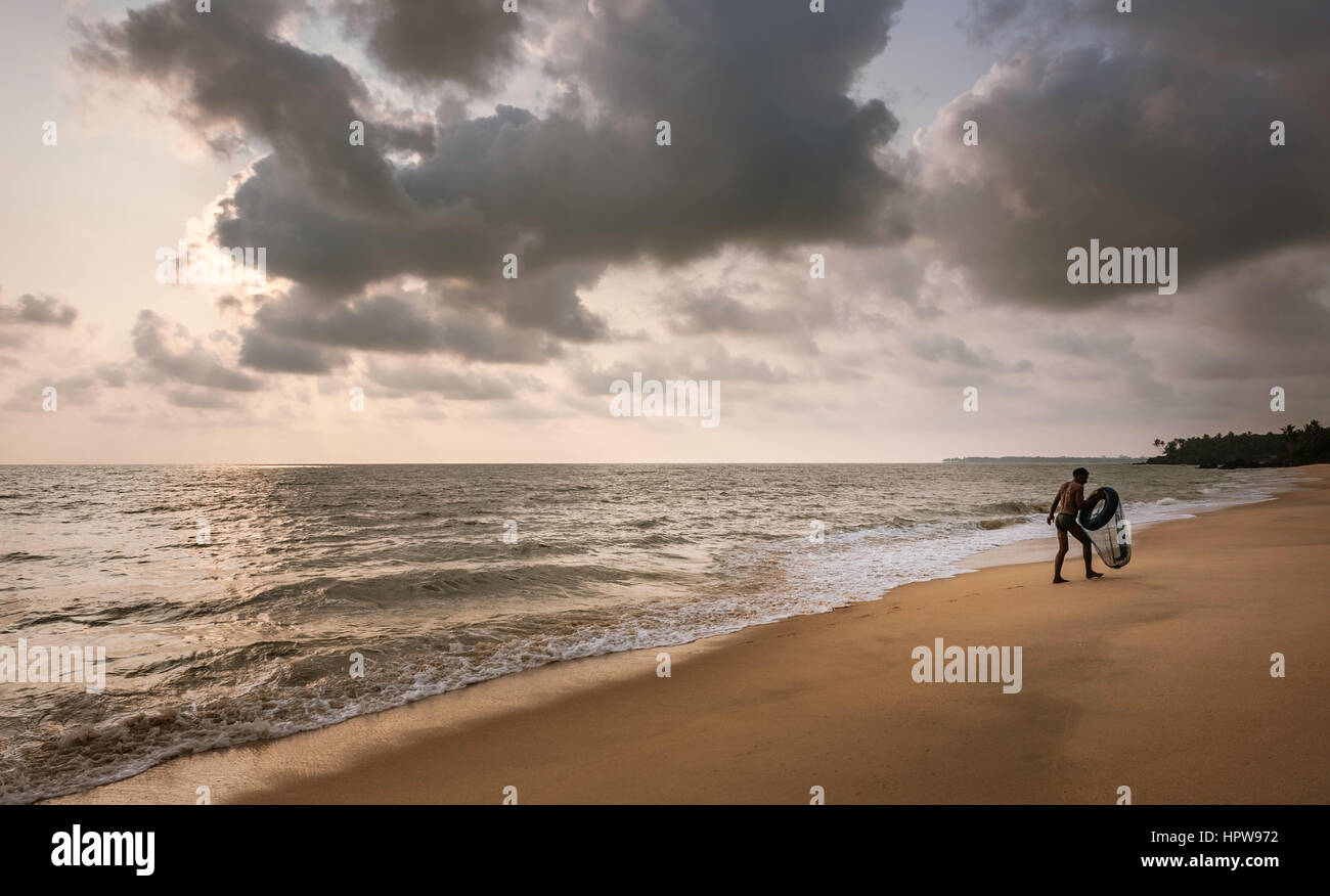 Ein Taucher für Weichtiere ergibt sich aus dem Meer mit seinen Reifen Schwimmer und Net entlang des Strandes mit Blick auf Arabische Meer bei Sonnenuntergang in der Nähe von Kannur, Kerala, Indien. Stockfoto