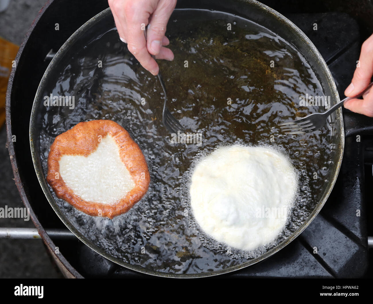 Händen der Kochen Braten zwei großer Pfannkuchen in einen Topf mit heißem Öl in einer Straße Imbiss-stand Stockfoto