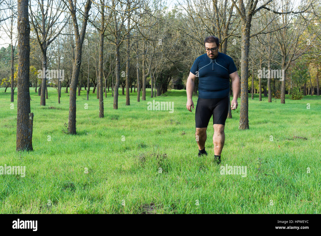 Dicken Bauch Mann Joggen, Sport treiben, tun, Cardio im Park, leicht übergewichtig, Gewicht zu verlieren. Auf einer Wiese grüne Gras zwischen den Bäumen ohne lea Stockfoto
