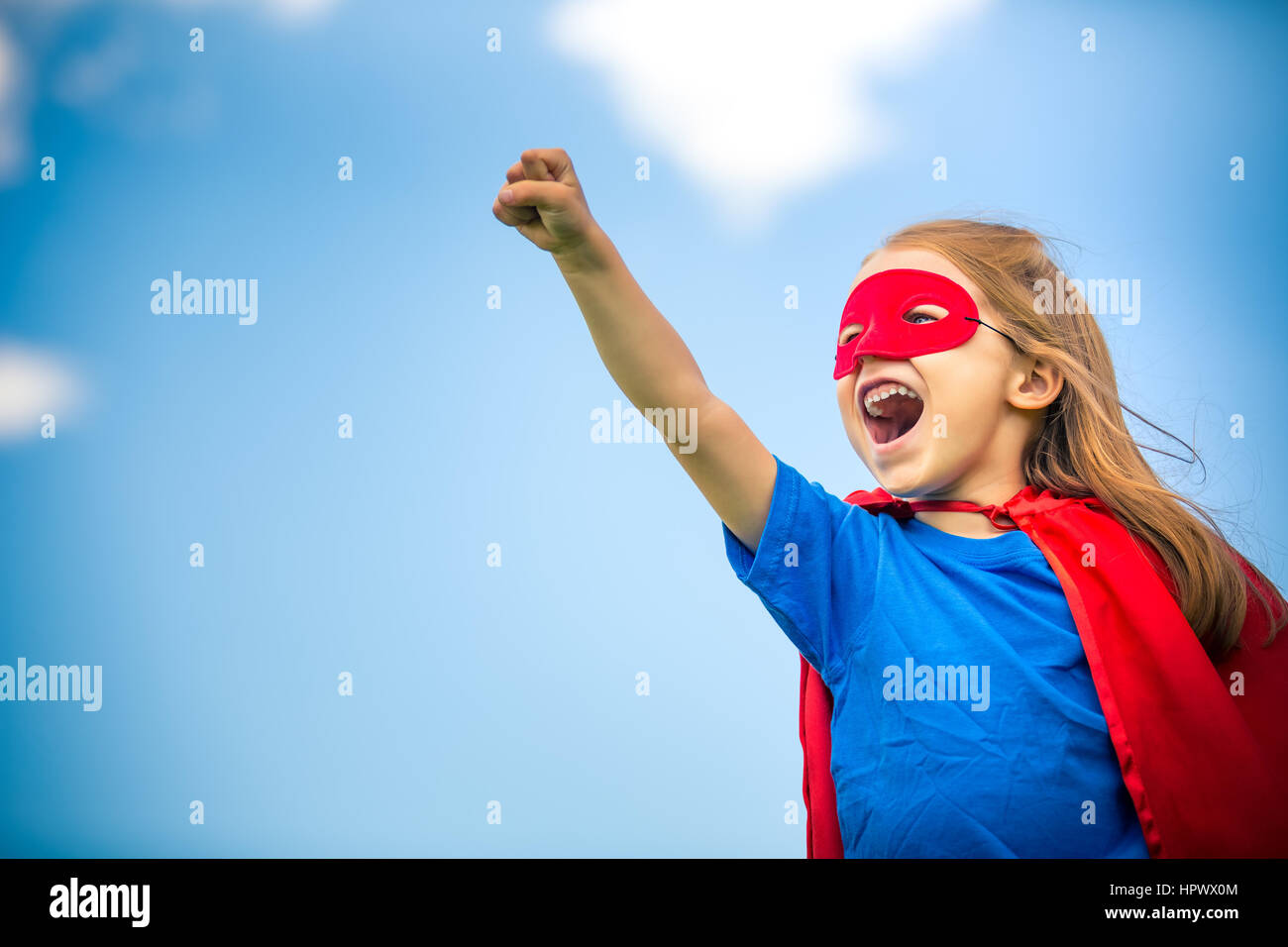 Lustiges kleines Mädchen macht super Hero über blauen Himmelshintergrund spielen. Superhelden-Konzept. Stockfoto