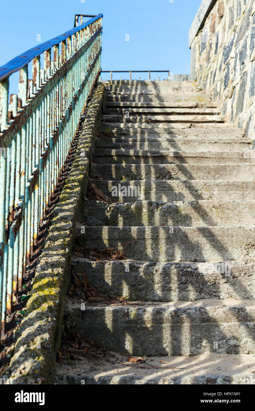 Verlassene Treppe mit Beton Trittsteine und Metall Handläufe, von der Sonne beleuchtet. Ansicht von unten auf. Sonniger Tag. Stockfoto