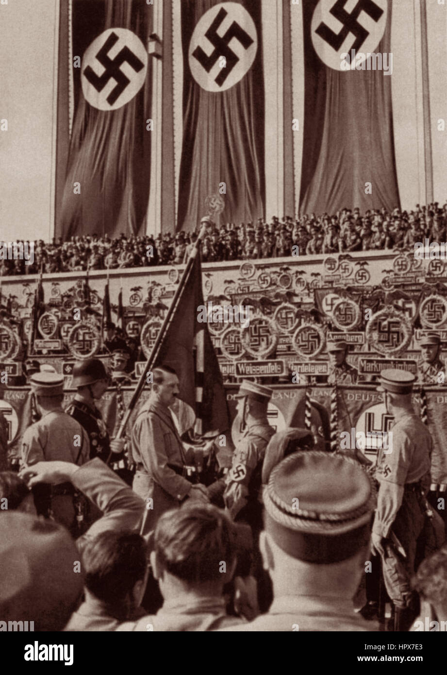 Adolf Hitler im Jahr 1934 am Reichsparteitag (nationalen Parteitag) Händeschütteln w / Soldat auf Stein Terrasse von Hall of Honor unter Hakenkreuz-Fahnen. Stockfoto