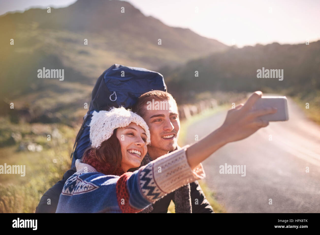Junges Paar mit Rucksack wandern nehmen Selfie mit Kamera-Handy auf sonnigen, abgelegenen Straße Stockfoto