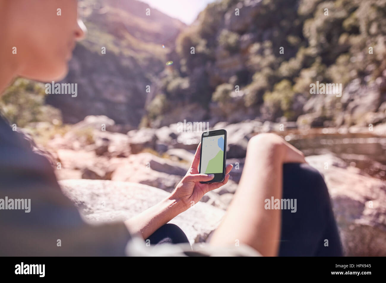 Junge Frau, die digitale Karte auf Smartphone an sonnigen Stream Anzeigen Stockfoto