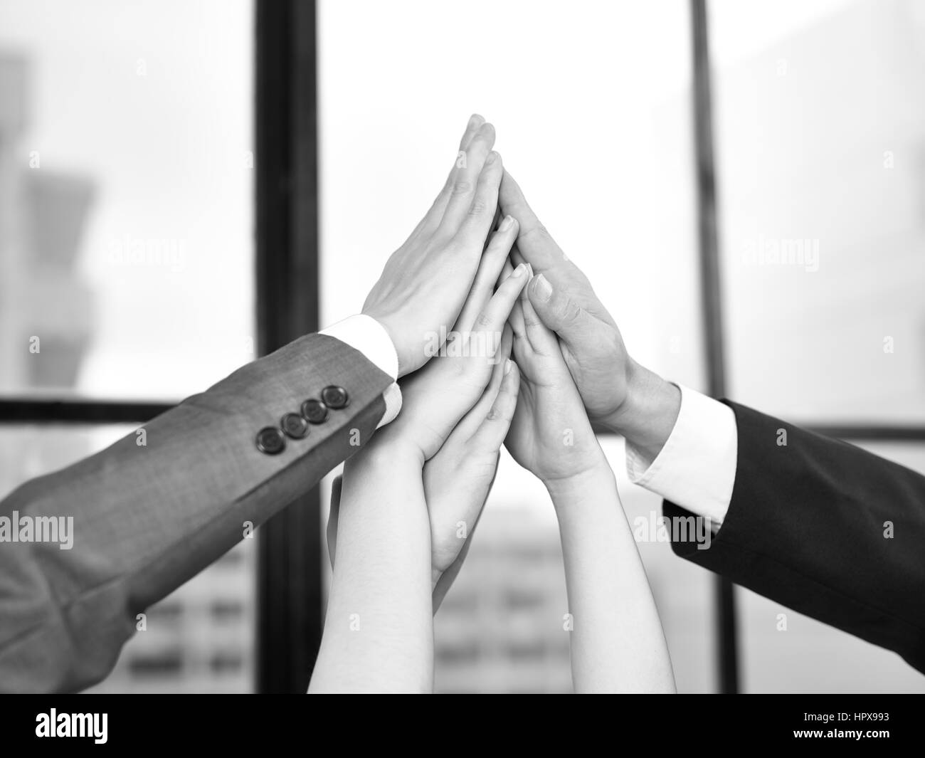 Geschäftsleute, die Hände zusammen, um eine Pyramide in einer Darstellung von Teamgeist und Entschlossenheit, schwarz und weiß bilden. Stockfoto