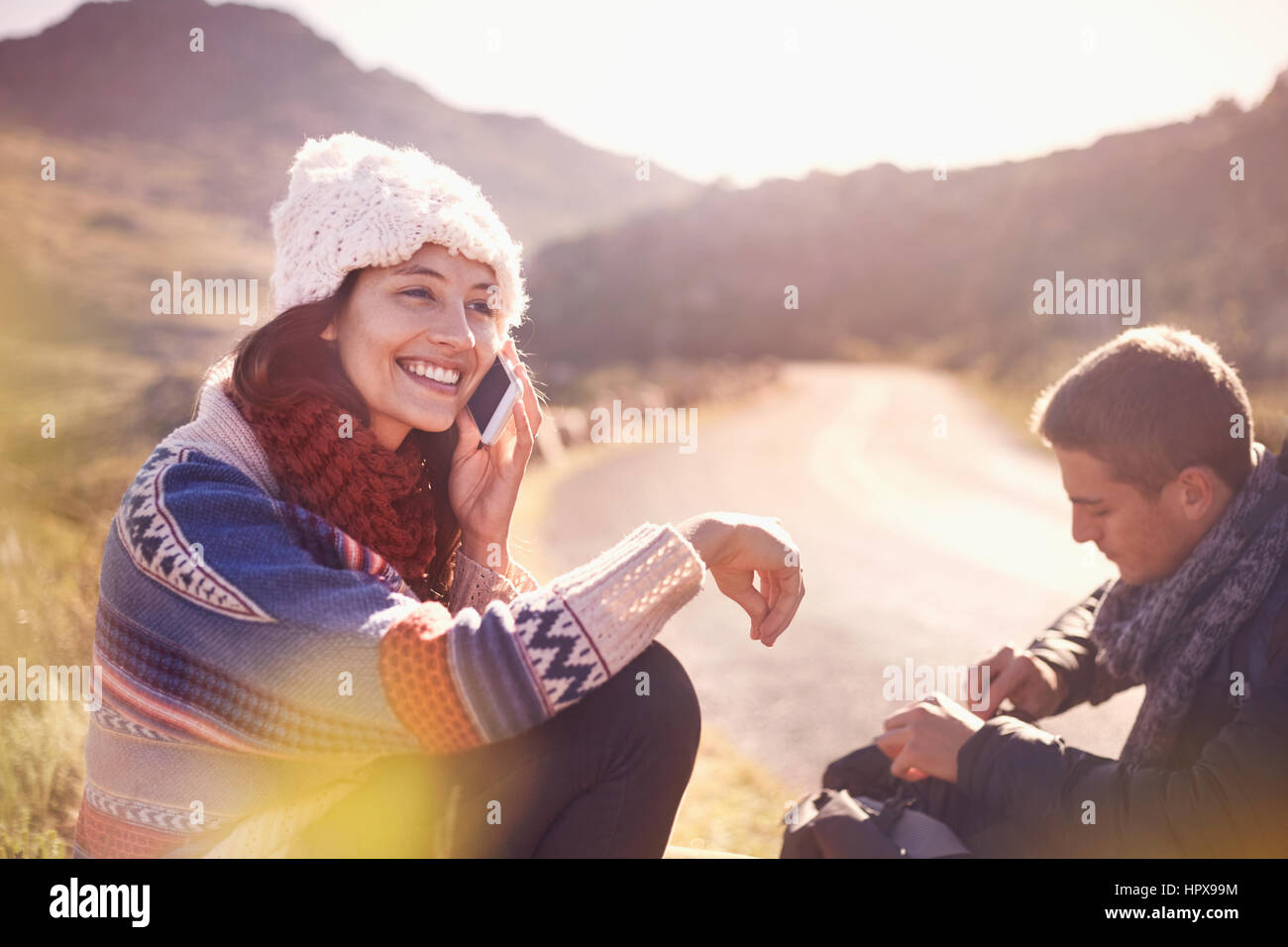 Lächelnde junge Frau am Handy auf sonnigen, abgelegenen Straße Stockfoto