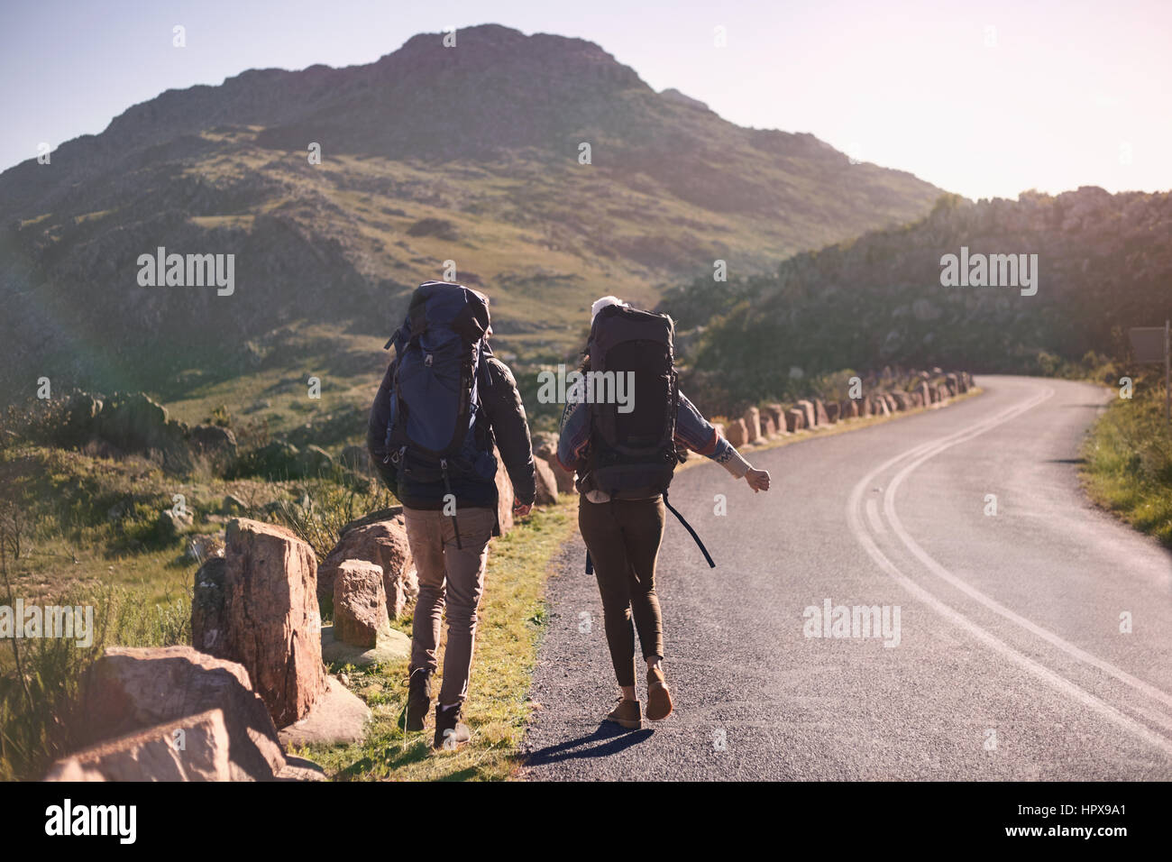 Junges Paar mit sonnigen, entfernten Straßenrand Wandern Rucksäcke Stockfoto