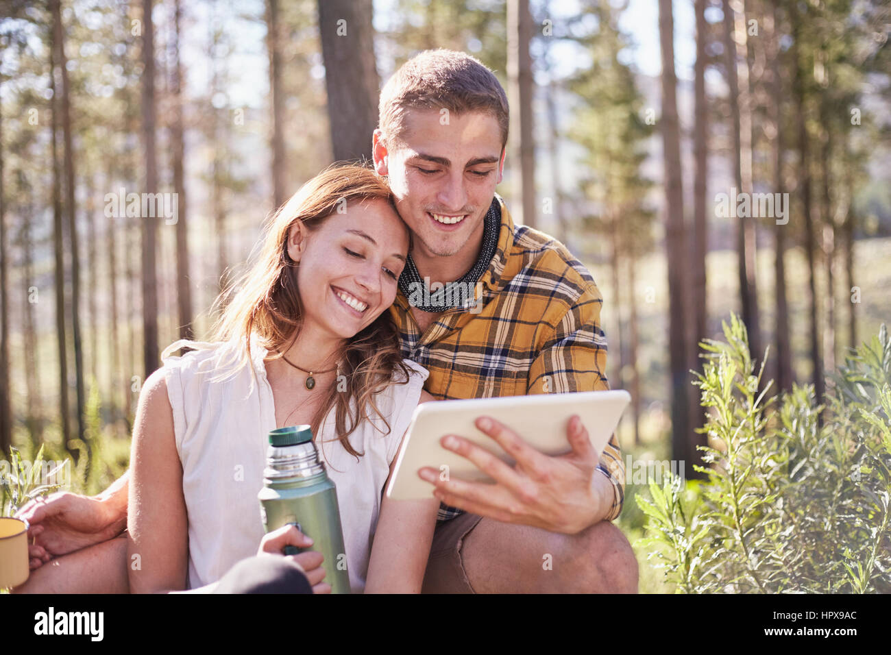 Junges Paar, camping, trinken Kaffee und mit digital-Tablette im sonnigen Wald Stockfoto