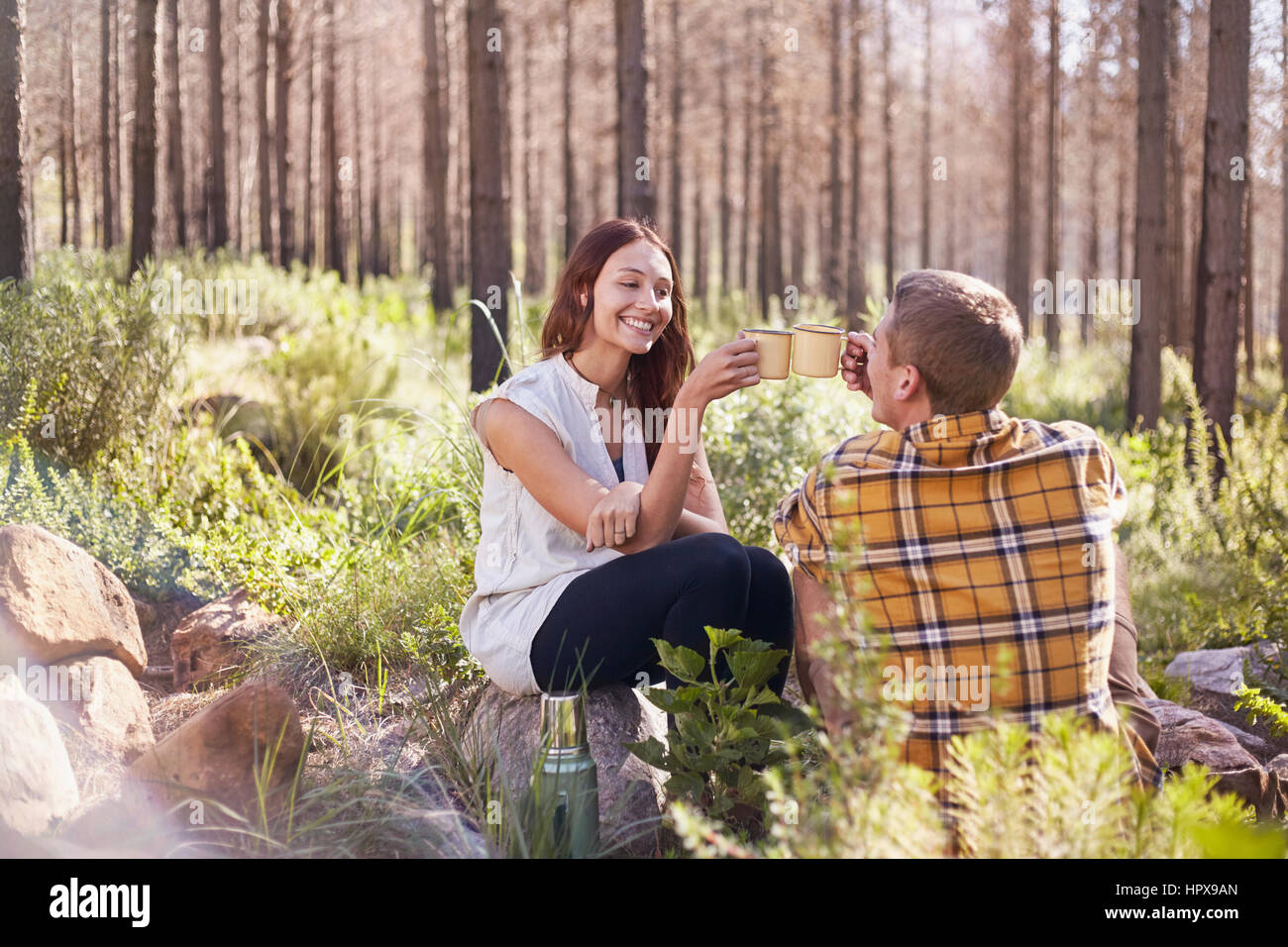 Junges Paar camping, toasten Kaffeetassen im sonnigen Wald Stockfoto