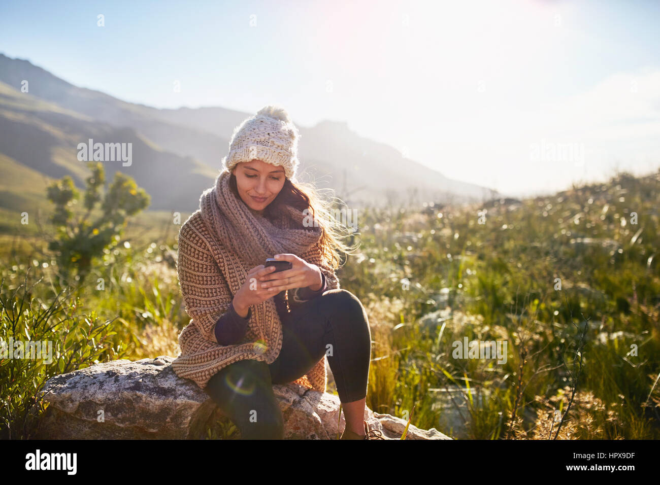 Junge Frau SMS mit Handy auf Felsen im sonnigen, abgelegenen Bereich Stockfoto